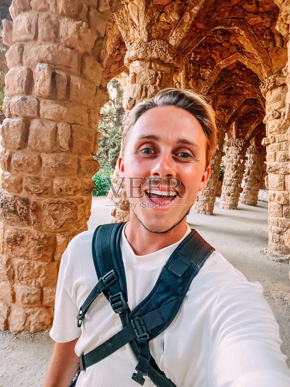 西班牙巴塞罗那，一位帅气、微笑的年轻人在格尔公园的柱子前自拍照片摄影图片