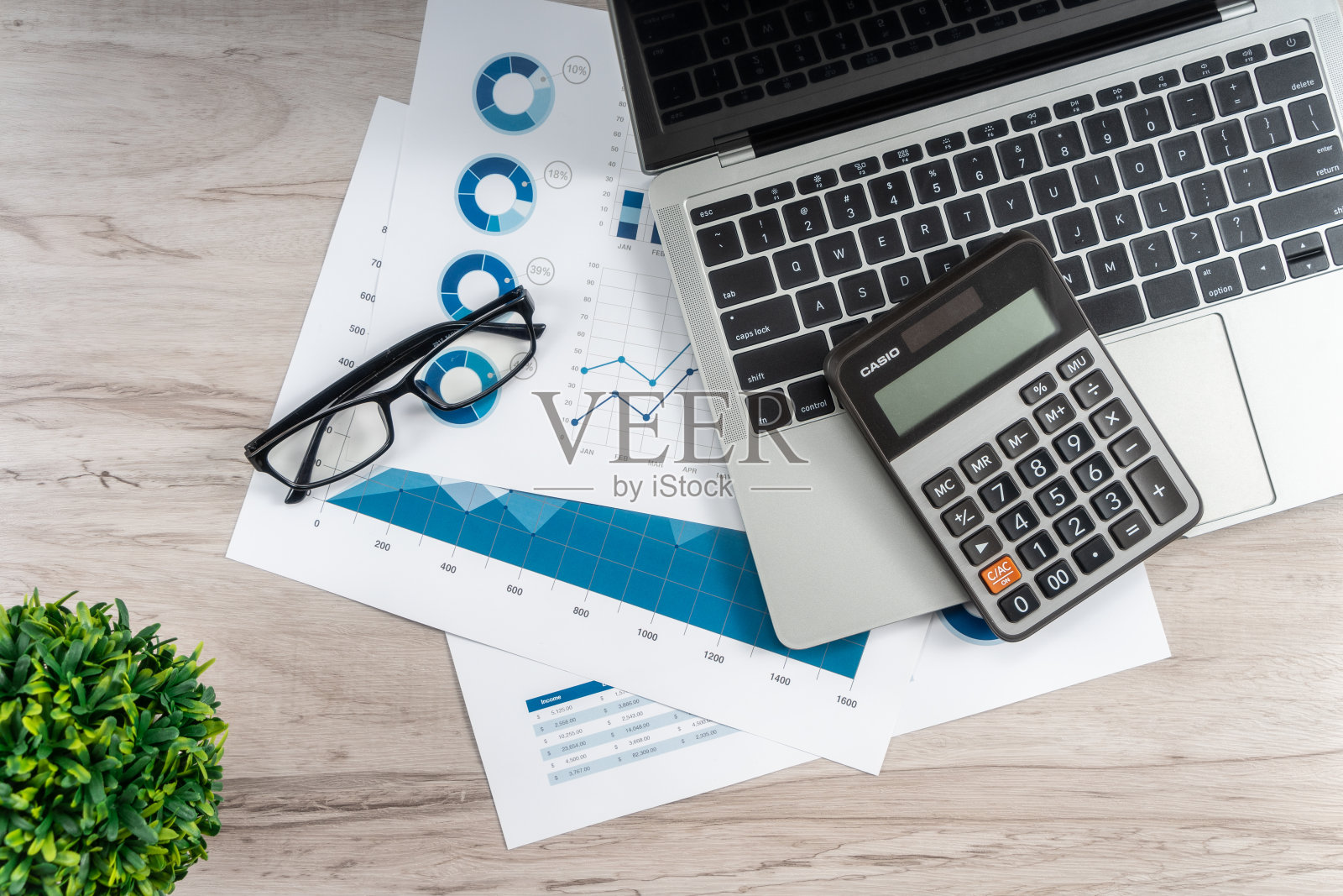 办公桌上有笔记本电脑，眼镜和财务图表。照片摄影图片