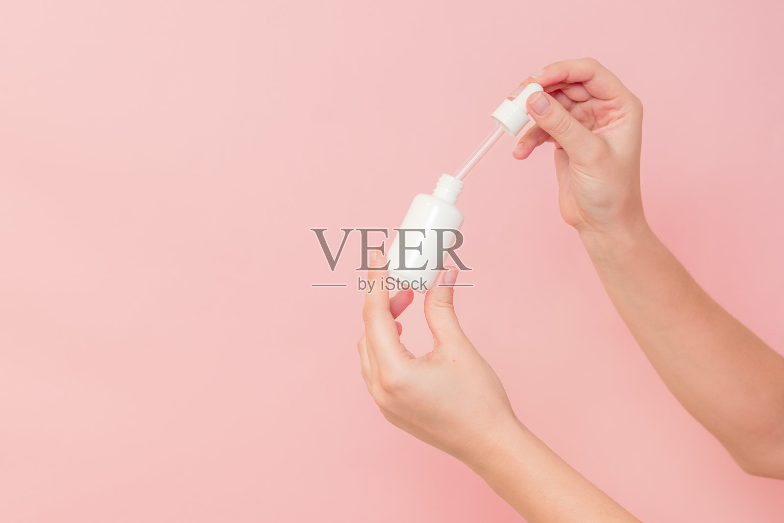 手持玻璃化妆品瓶血清(透明质酸和胶原蛋白)在粉红色的背景。美丽的概念照片摄影图片