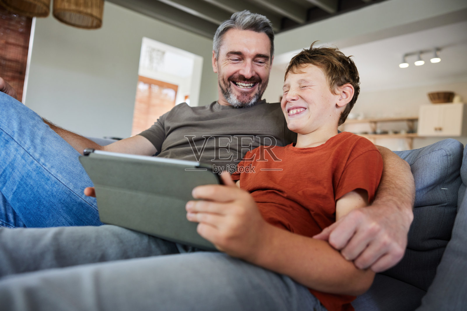 爸爸和儿子坐在家里，对着平板电脑笑个不停照片摄影图片