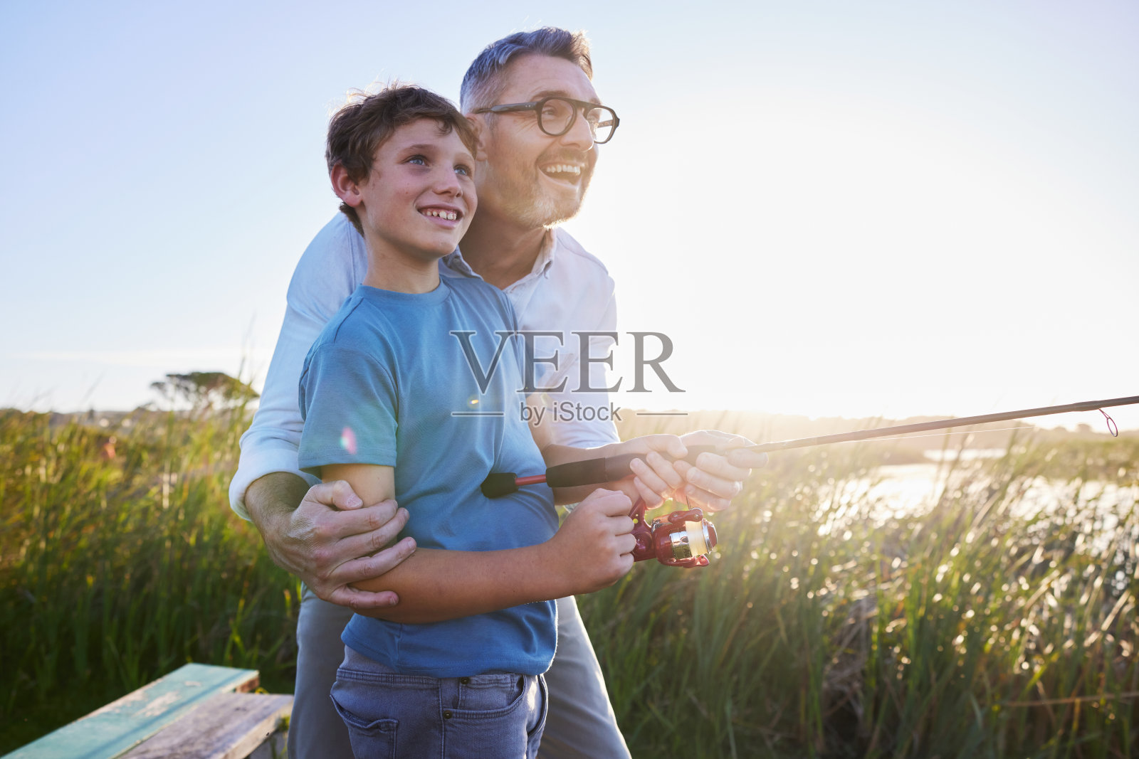 微笑的爸爸在风景优美的湖边教他年幼的儿子如何钓鱼照片摄影图片