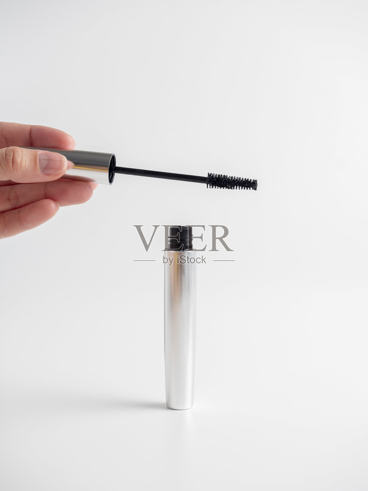 女人的手握着白色背景上的睫毛膏。涂睫毛膏的刷子。化妆品的概念照片摄影图片