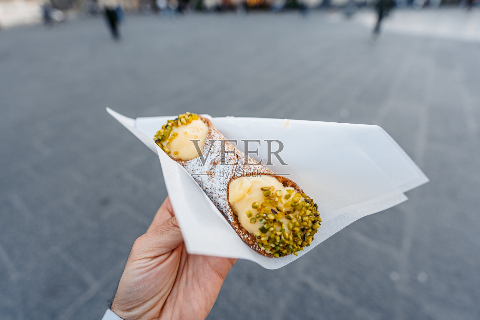 在西西里岛卡塔尼亚的街道上，年轻人拿着奶油乳清干酪和开心果馅的煎饼卷照片摄影图片