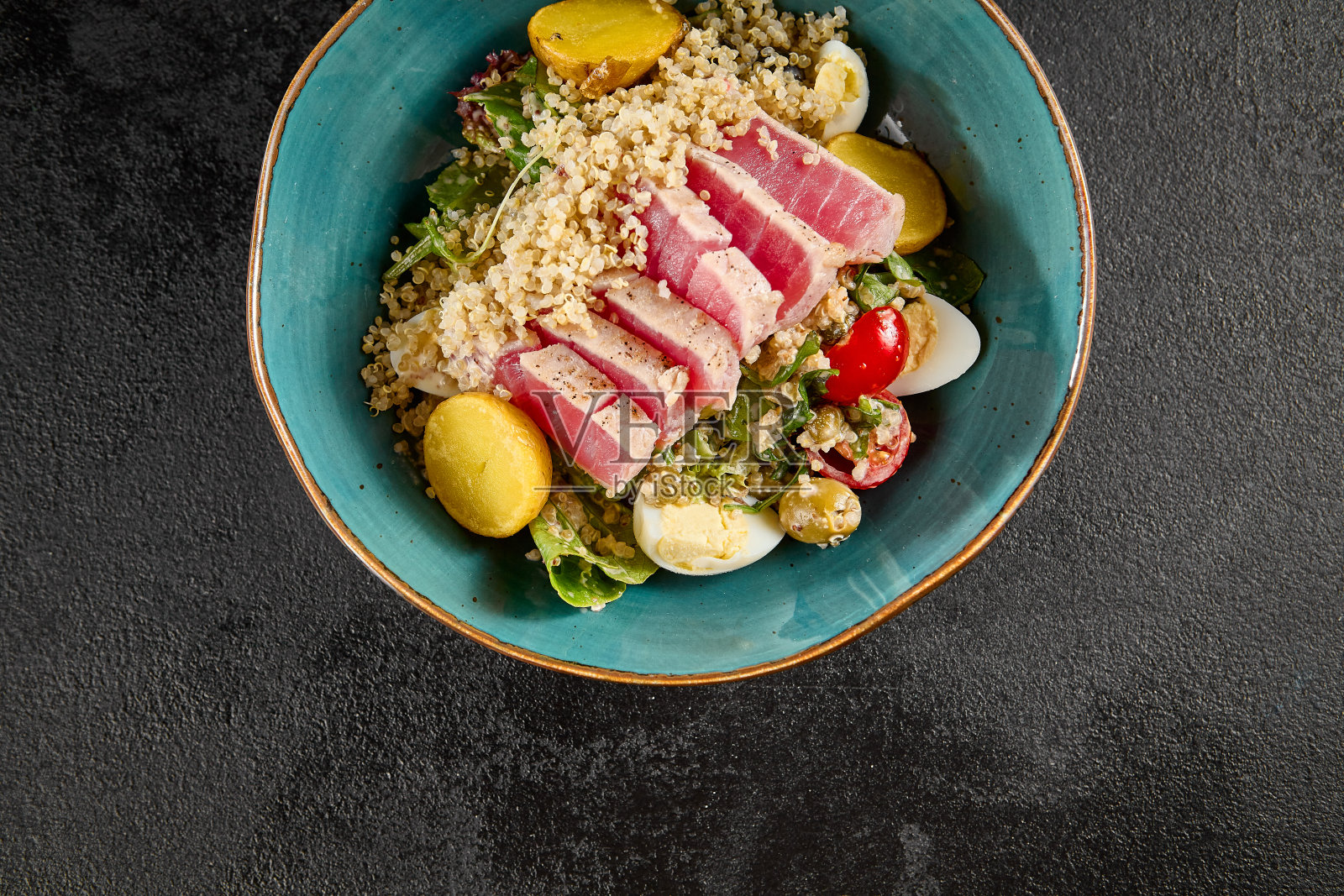 一个奎奴亚藜碗的俯视图与中等烤金枪鱼，混合蔬菜，和柠檬角，在一个绿松石陶瓷盘子照片摄影图片