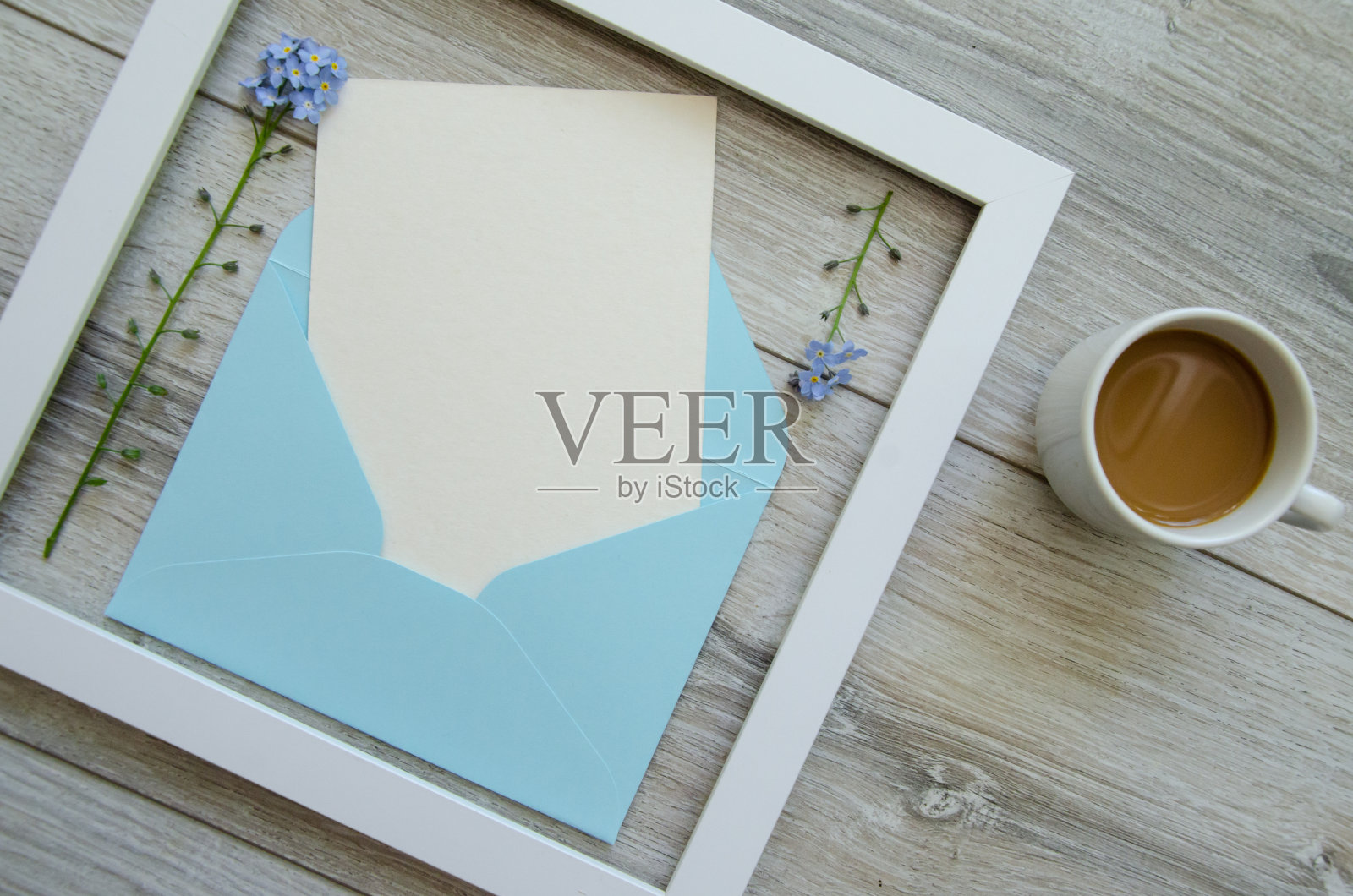 平坦的灰色自然木制背景，方形白色木框和蓝色信封，白色明信片的文案空间，小黄花和树枝上的绿叶照片摄影图片