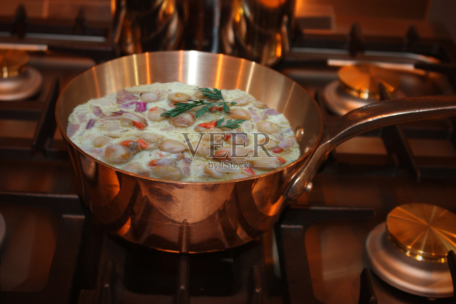 在煤气灶上的铜锅里用奶油煮扇贝照片摄影图片