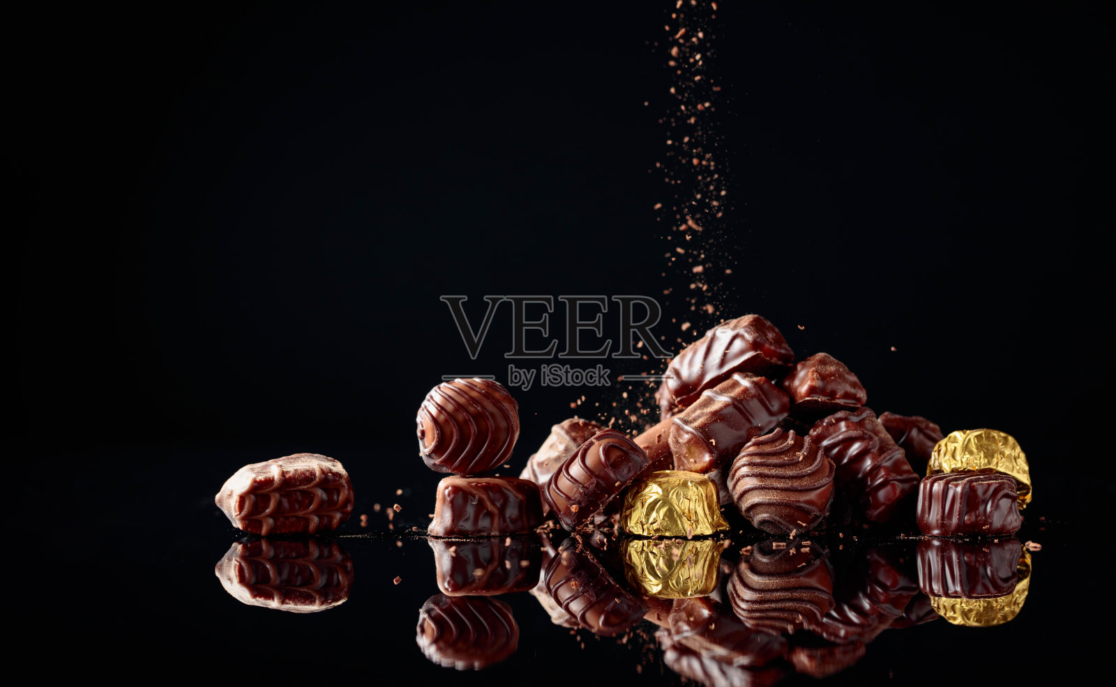 各种各样的巧克力糖果在黑色的背景上洒上巧克力片。照片摄影图片