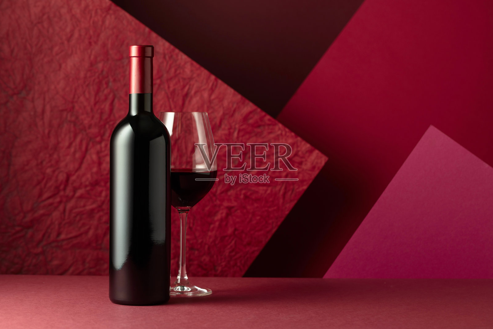 一瓶和一杯红色背景的红酒。照片摄影图片