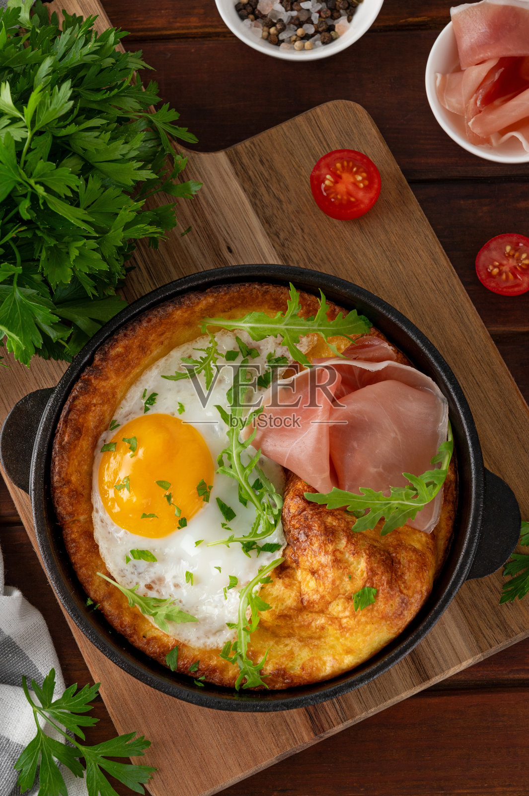 美味的荷兰婴儿煎饼与奶酪，煎蛋，芝麻菜和熏火腿在铸铁锅在深色木制背景。照片摄影图片