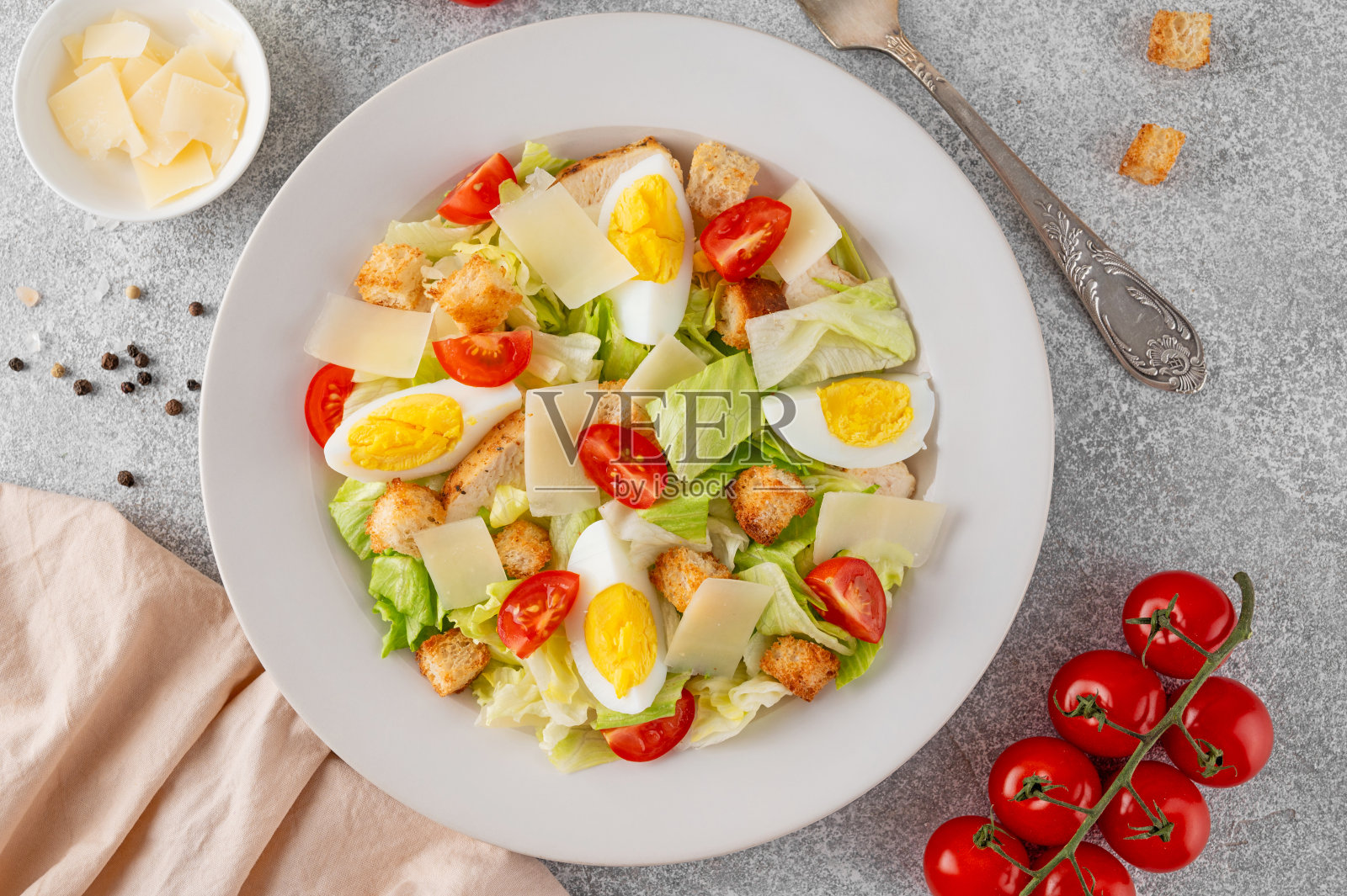 凯撒沙拉，有生菜、烤鸡胸肉、煮鸡蛋、西红柿、帕尔马干酪和面包丁，放在混凝土背景上的陶瓷盘子里。前视图。照片摄影图片