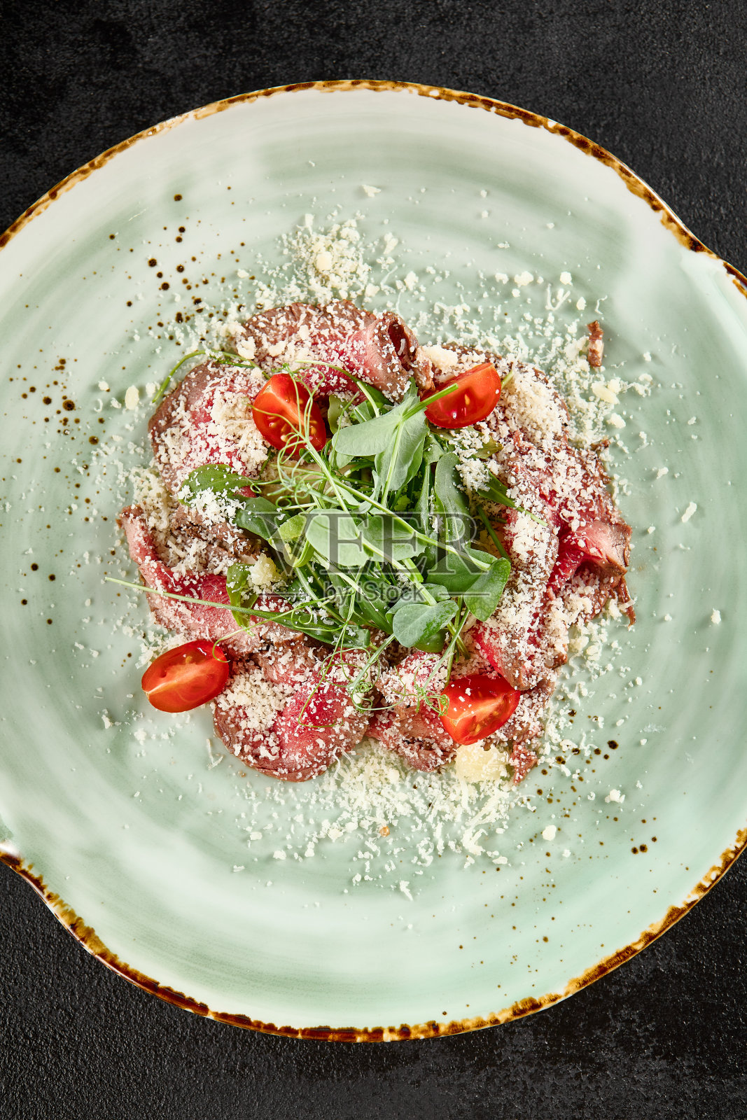 烤牛肉配帕尔马干酪屑、芝麻菜和绿松石盘子里的半切圣女果照片摄影图片