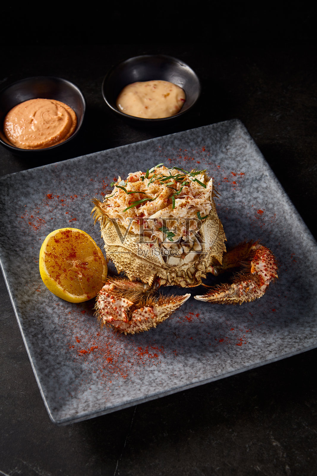 清洗过的蟹肉加柠檬的特写，放在大闸蟹里，用灰色的石头盘子盛着酱汁，黑色背景照片摄影图片