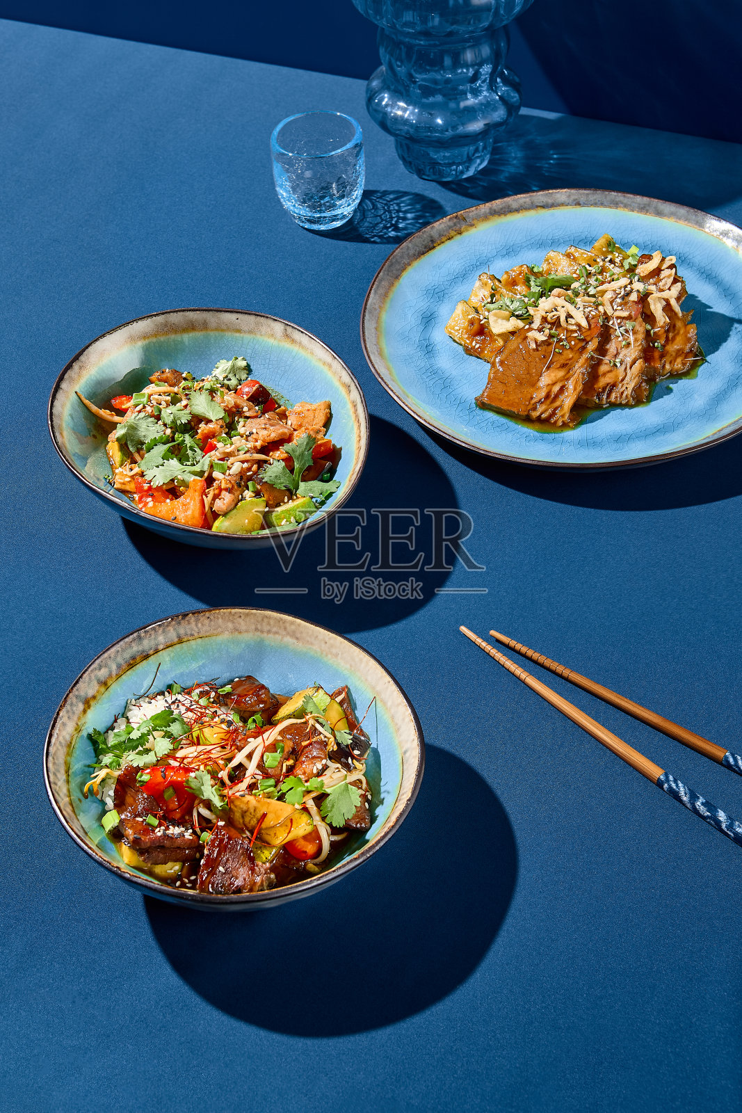 亚洲风格的一套肉菜的侧视图，极简主义的构图与阴影，伴随着筷子，在充满活力的蓝色背景下照片摄影图片