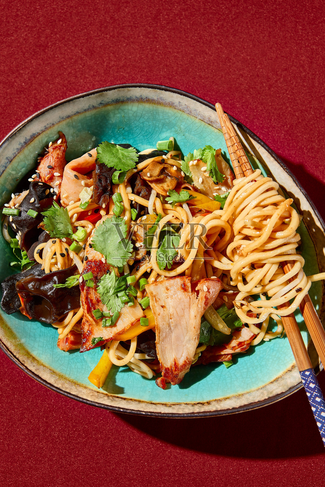 亚洲小麦面配鸡肉和木耳菇的特写。巧妙地装在陶瓷碗里，面条盘绕在筷子上。照片摄影图片