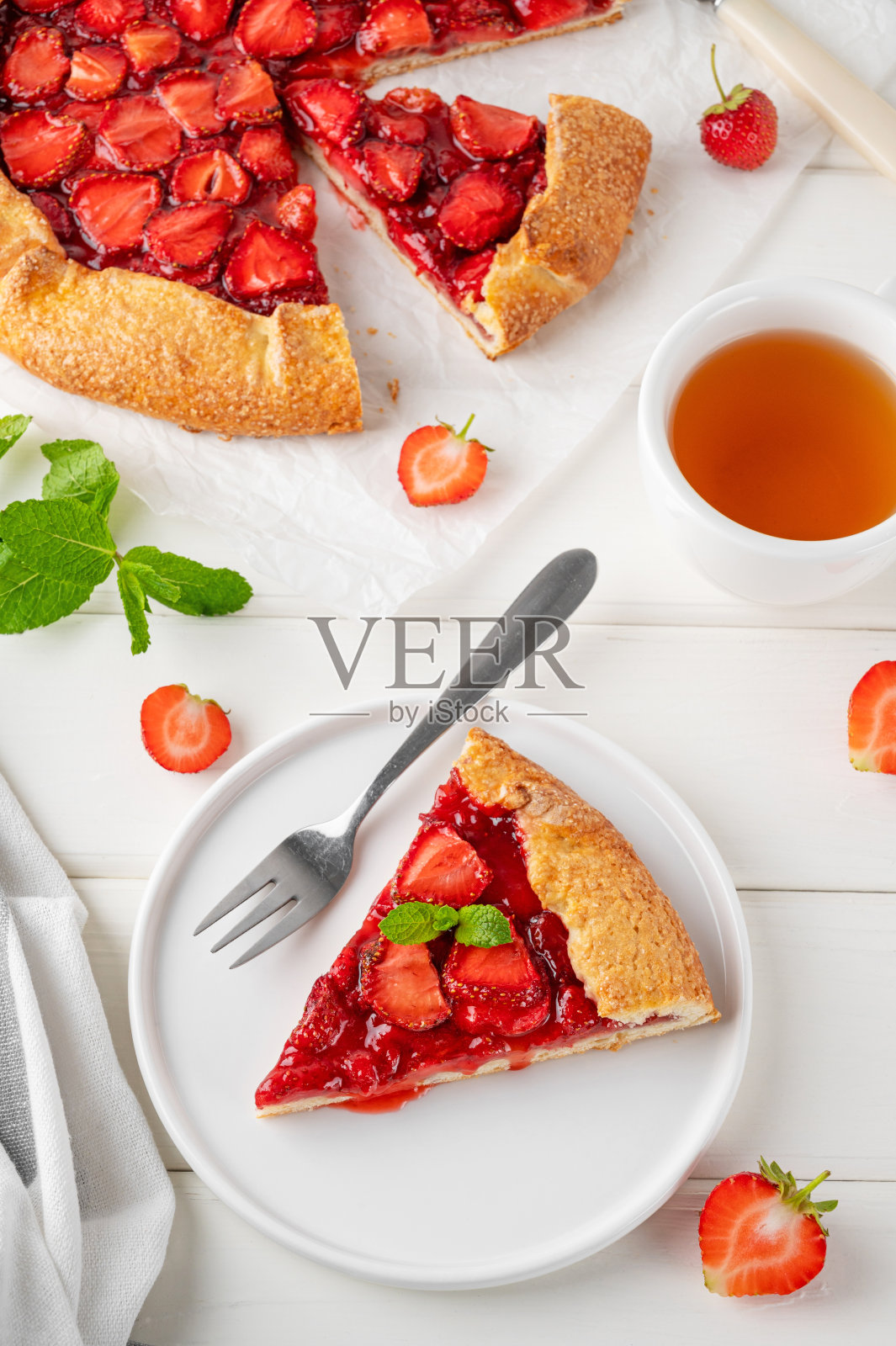 在白色的木桌上，你可以吃到开放式的馅饼或草莓馅饼，配上一杯茶。夏日甜派。照片摄影图片