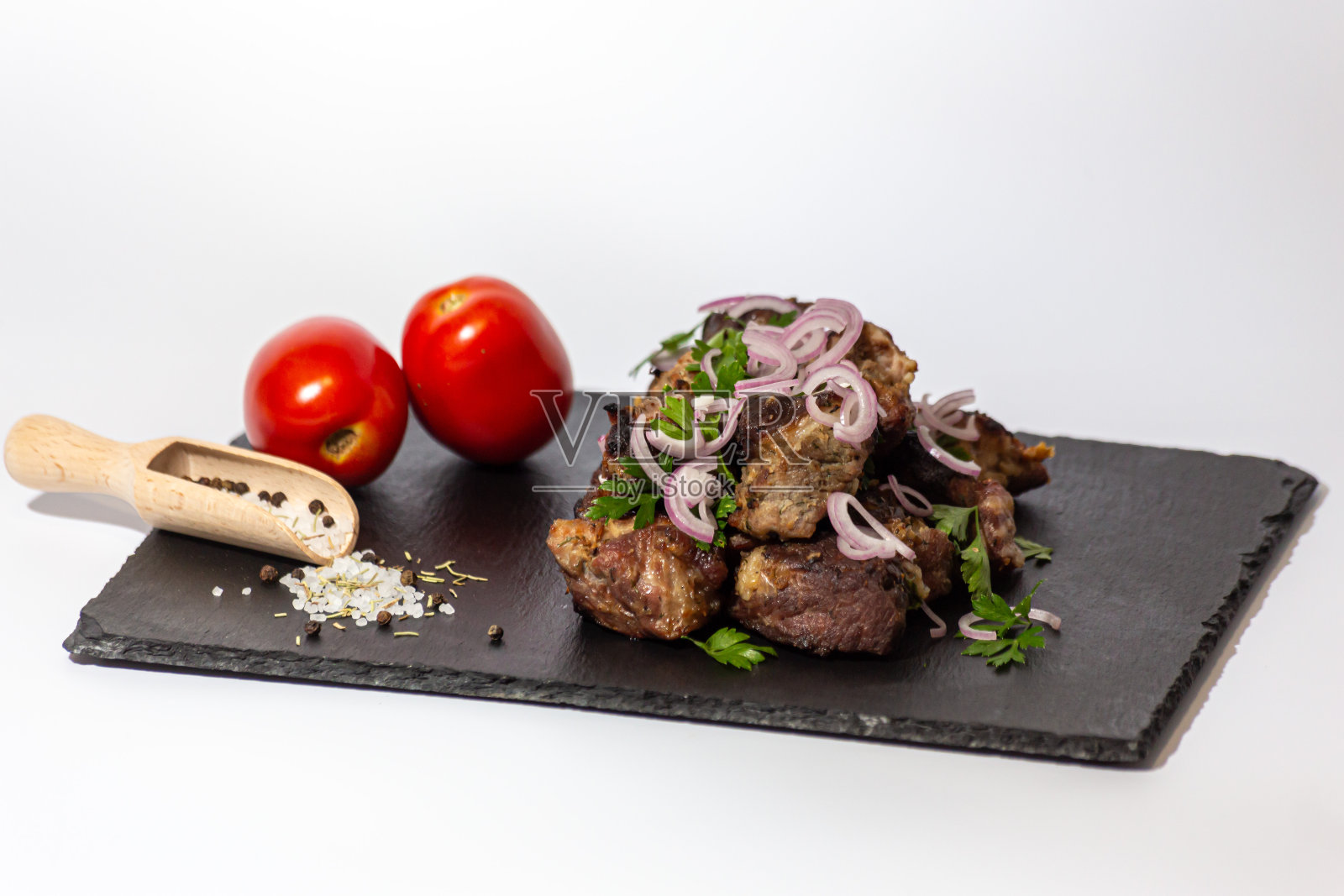 沙沙利克——将猪肉片与青葱、番茄和香草一起放在白底石板托盘上，在木炭上煎炸。照片摄影图片