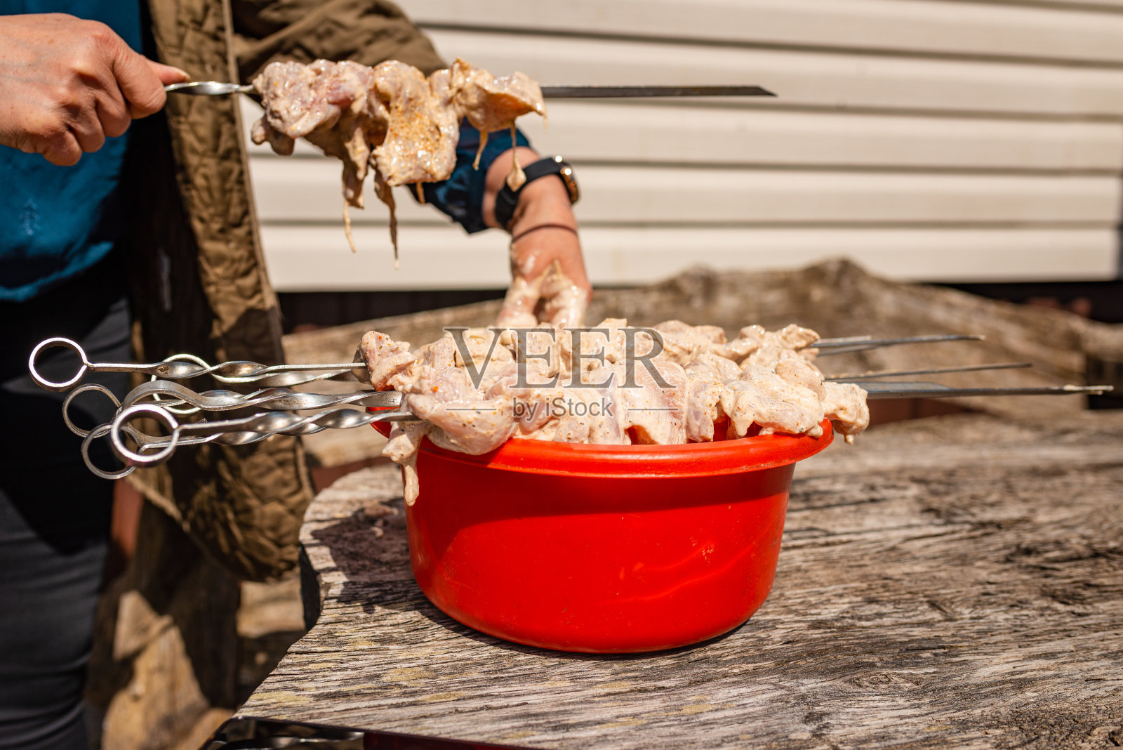 一名妇女用手将生猪肉刺穿在铝制金属盆里的叉子上，在户外烹饪鸡肉串。夏天美好的一天。照片摄影图片