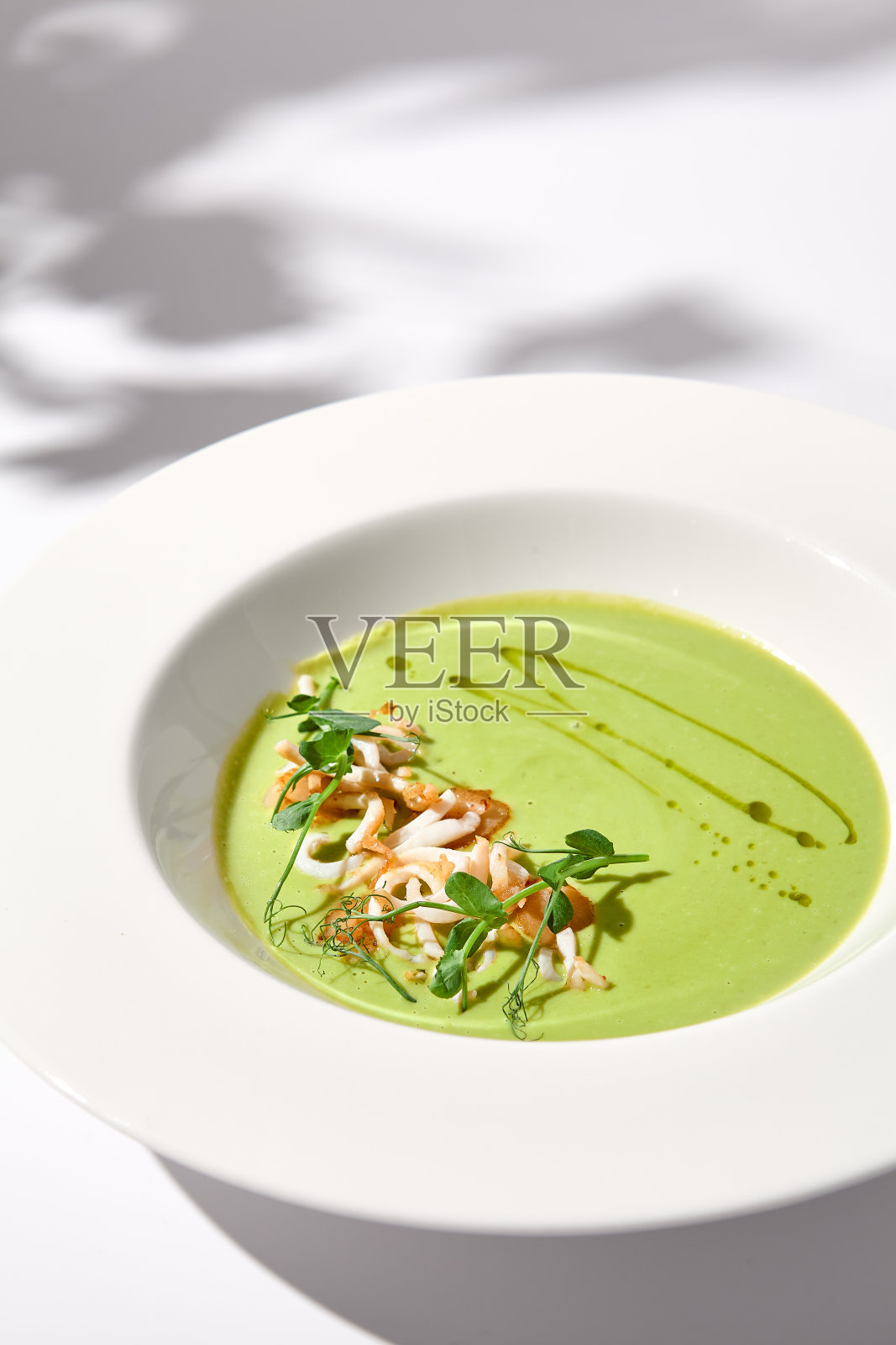 菠菜奶油汤加鱿鱼头，巧妙地呈现在一个白色的盘子与阴影，完美的美食广告照片摄影图片