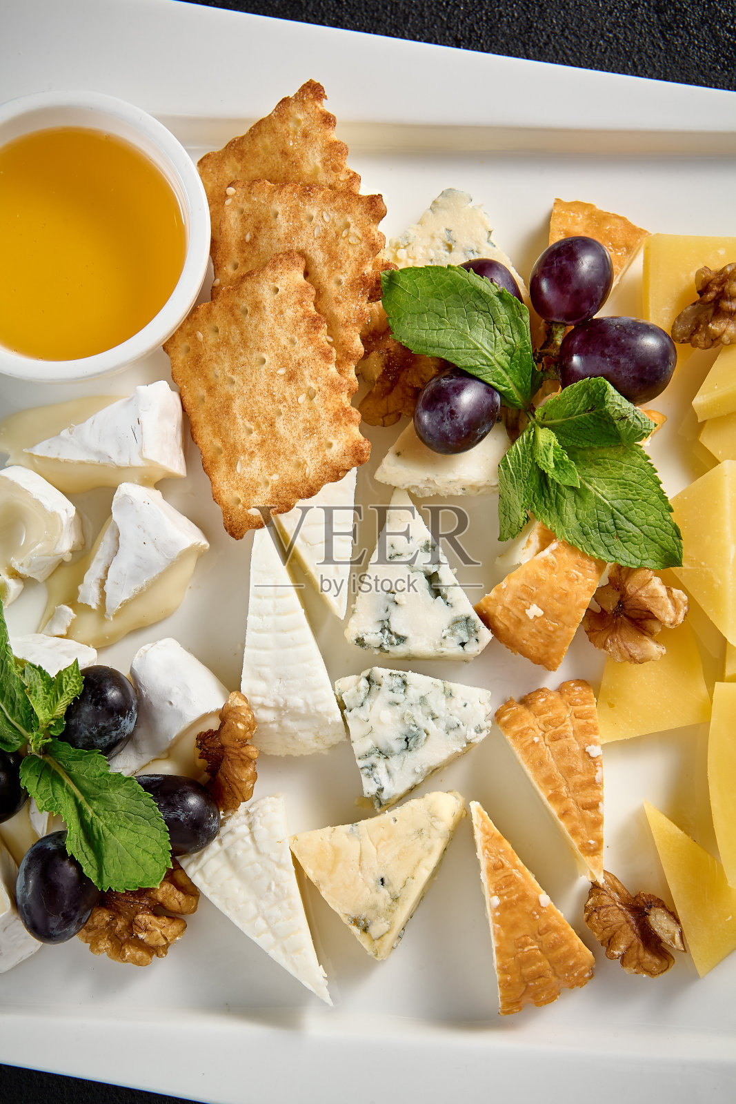 奶酪板，葡萄和蜂蜜在白色的盘子在黑色的背景照片摄影图片