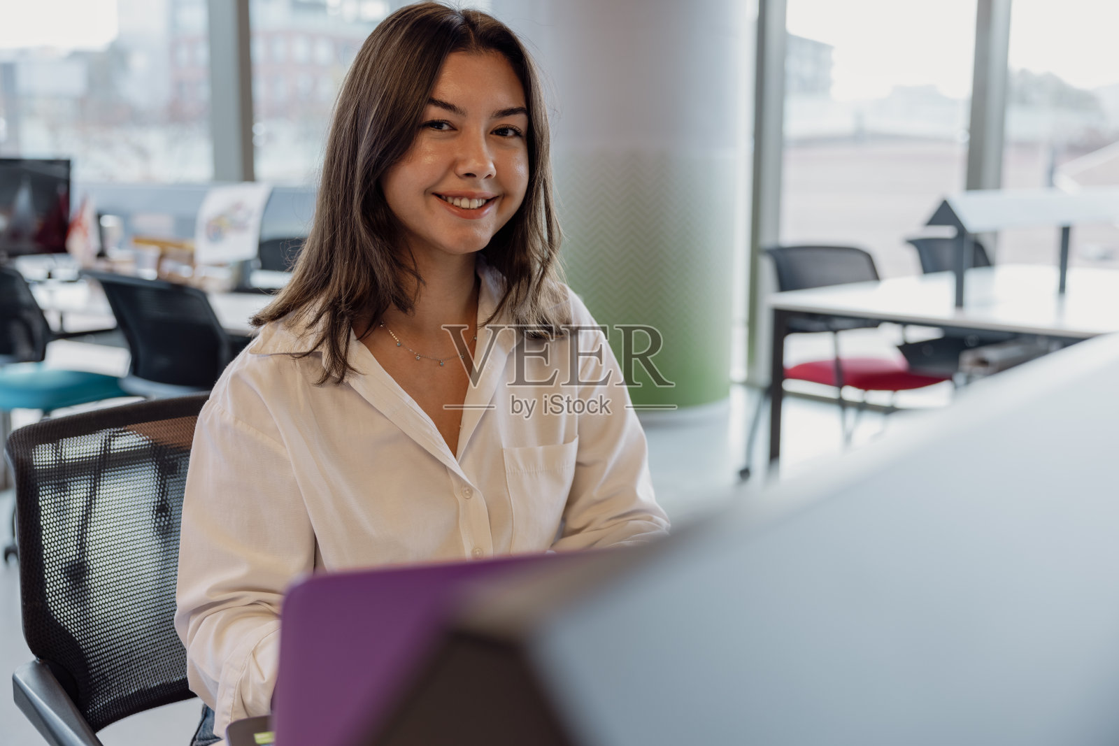 一个年轻的女商人、设计工作者或实习生坐在现代开放式办公室的电脑前。照片摄影图片