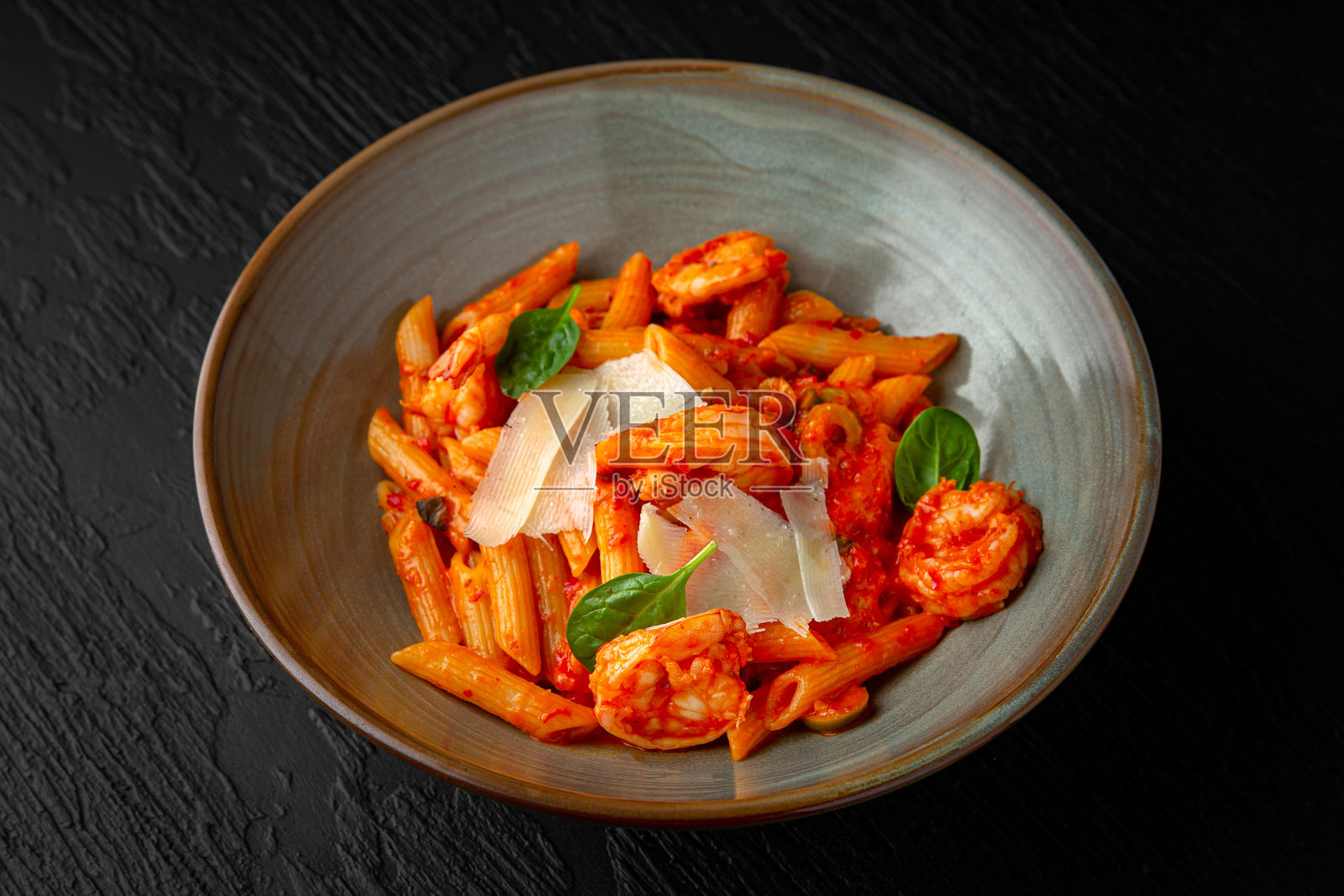 黑色纹理背景上的陶瓷盘子里有橄榄和虾。餐厅的菜单照片摄影图片