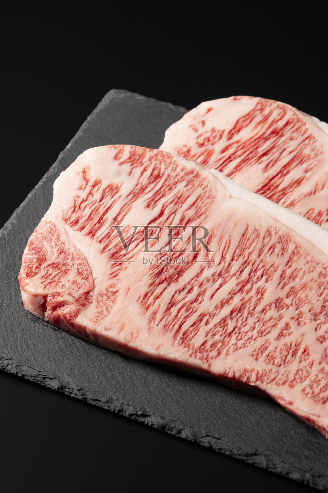 新鲜的生牛排放在黑背景的石盘上。和牛牛排。照片摄影图片