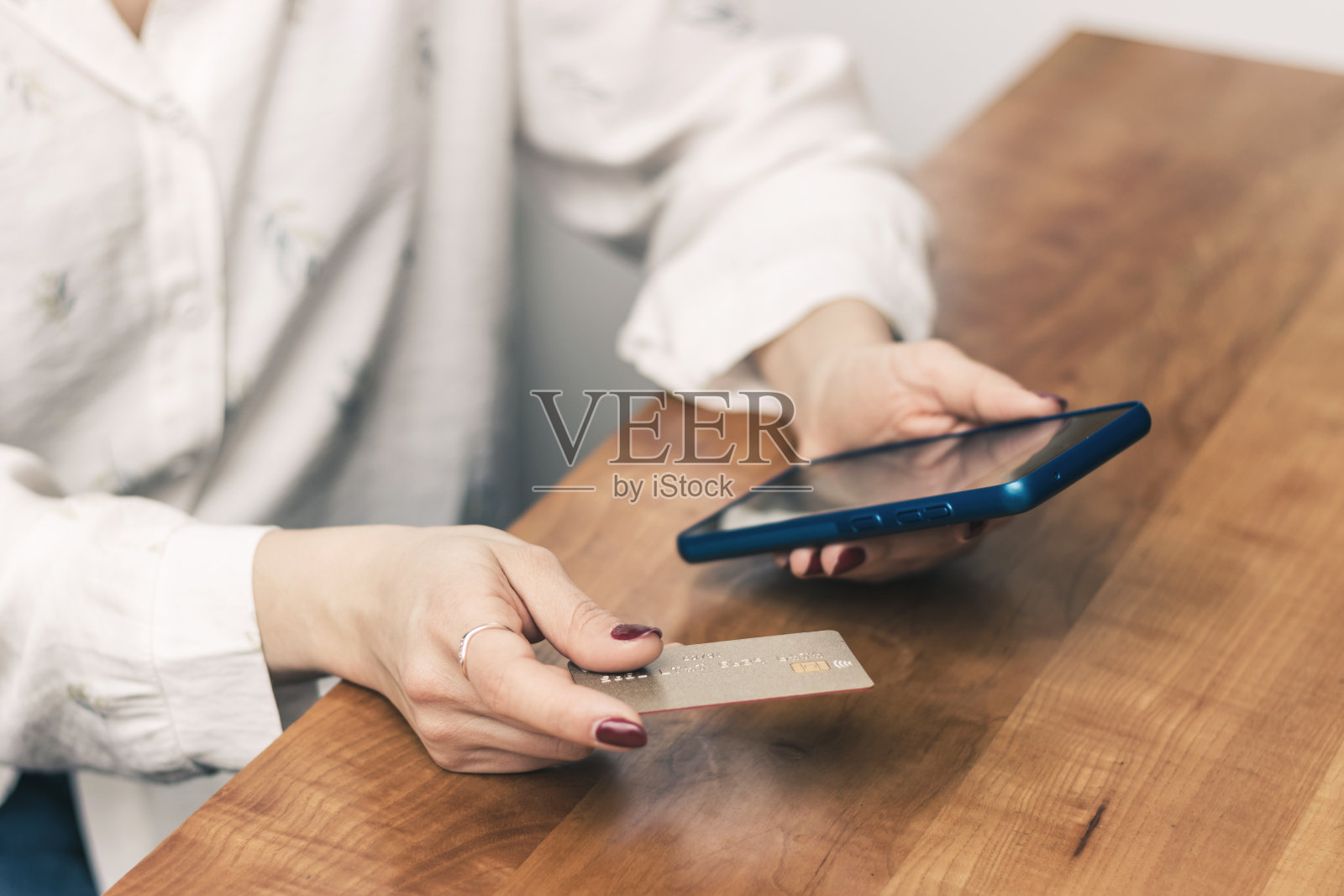 女人手里拿着信用卡，在桌子上使用手机进行网上购物、支付或工作照片摄影图片