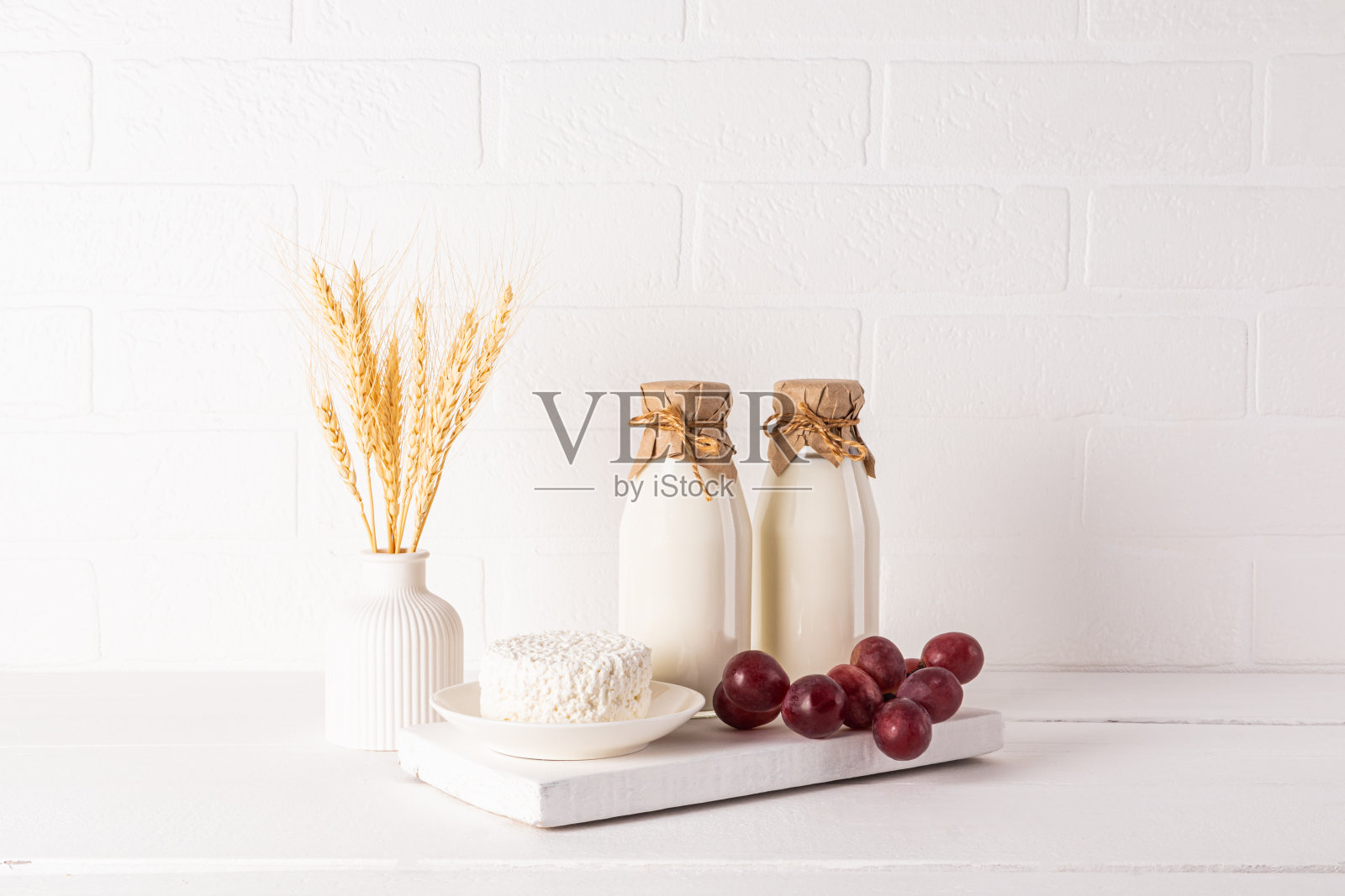 白色的木板上放着新鲜的奶制品，木桌上放着一个插着玉米穗的花瓶。犹太节日Shavuot的概念。生态风格照片摄影图片