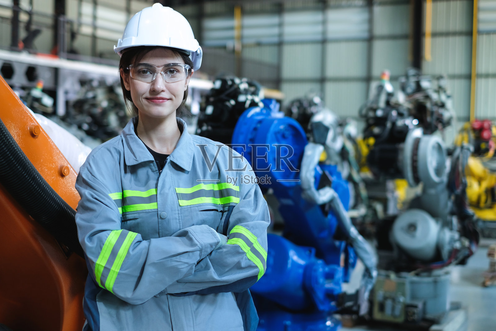 现代工厂里，戴着安全帽的女性自动化工程师与许多工业机器人手臂交叉站立。照片摄影图片
