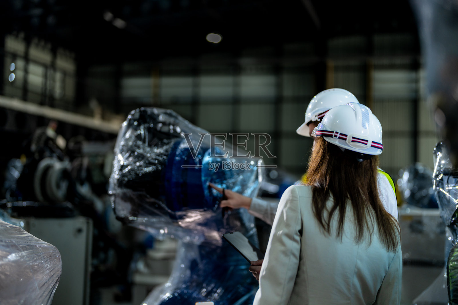 业务工程师开会并检查控制重型机械的机械臂。不同的工业机器人工程师团队聚集在机器周围。专业机械操作员使用工业数码平板电脑。照片摄影图片