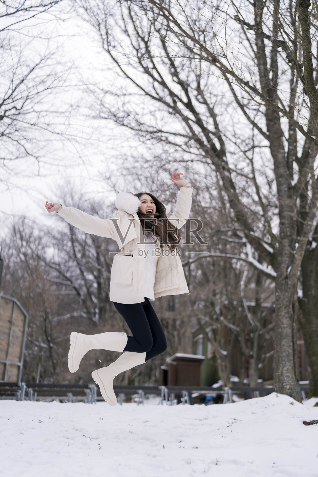 迷人的亚洲旅行者女性享受跳跃乐趣，无忧无虑，穿着冬衣，在雪地花园度过假期，清新愉快，享受旅行理念照片摄影图片