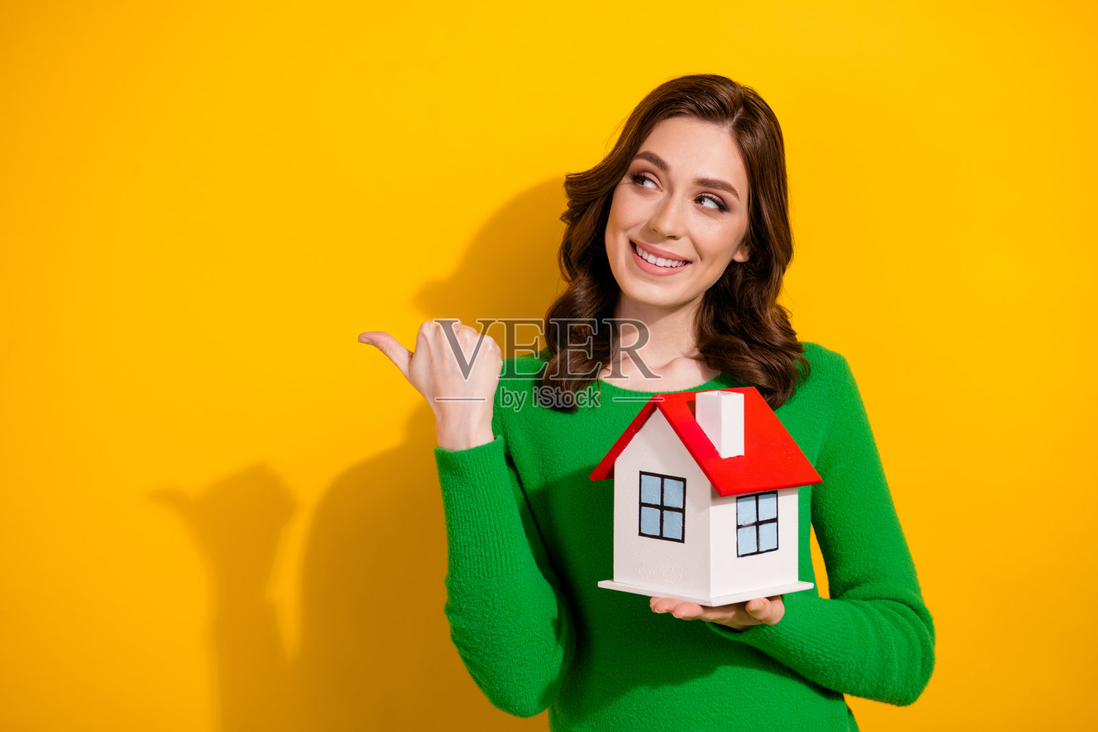 满意的女孩顾客穿着时尚的绿色套头衫的照片推荐住宅综合体空旷的空间孤立在黄色的背景照片摄影图片