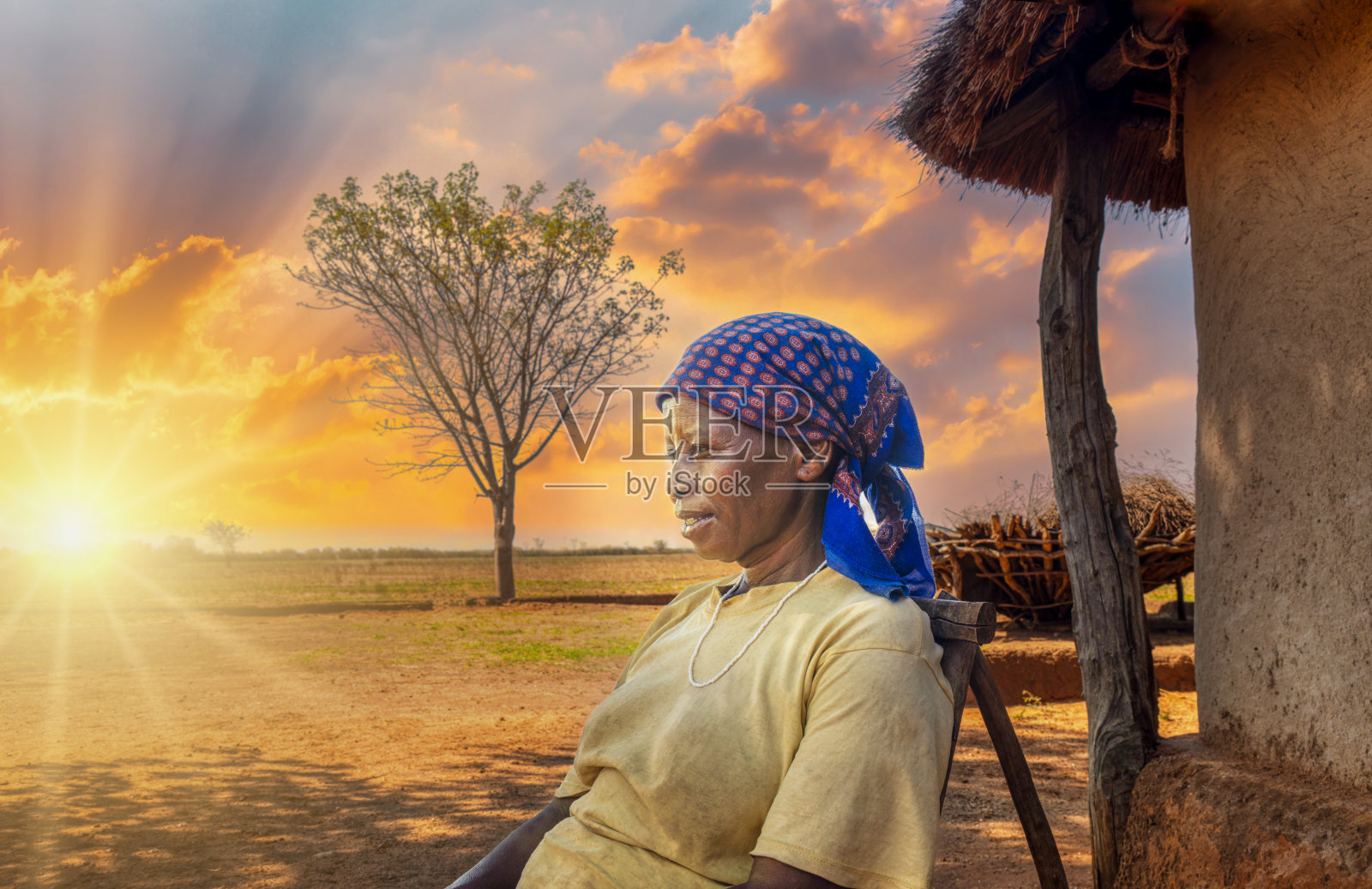 村庄里的非洲成年妇女，日落时分坐在院子里的一把椅子上，前面是一间茅草屋照片摄影图片