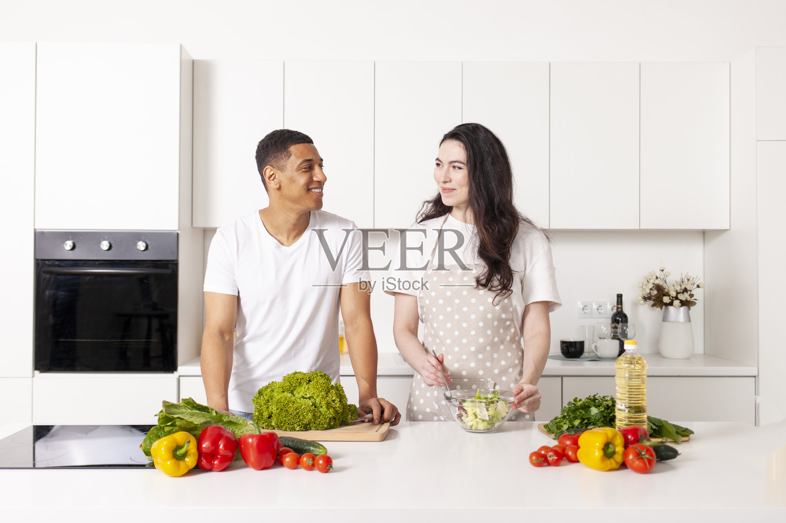 非裔美国男人和欧洲女人在白色厨房里一起准备蔬菜和蔬菜沙拉照片摄影图片