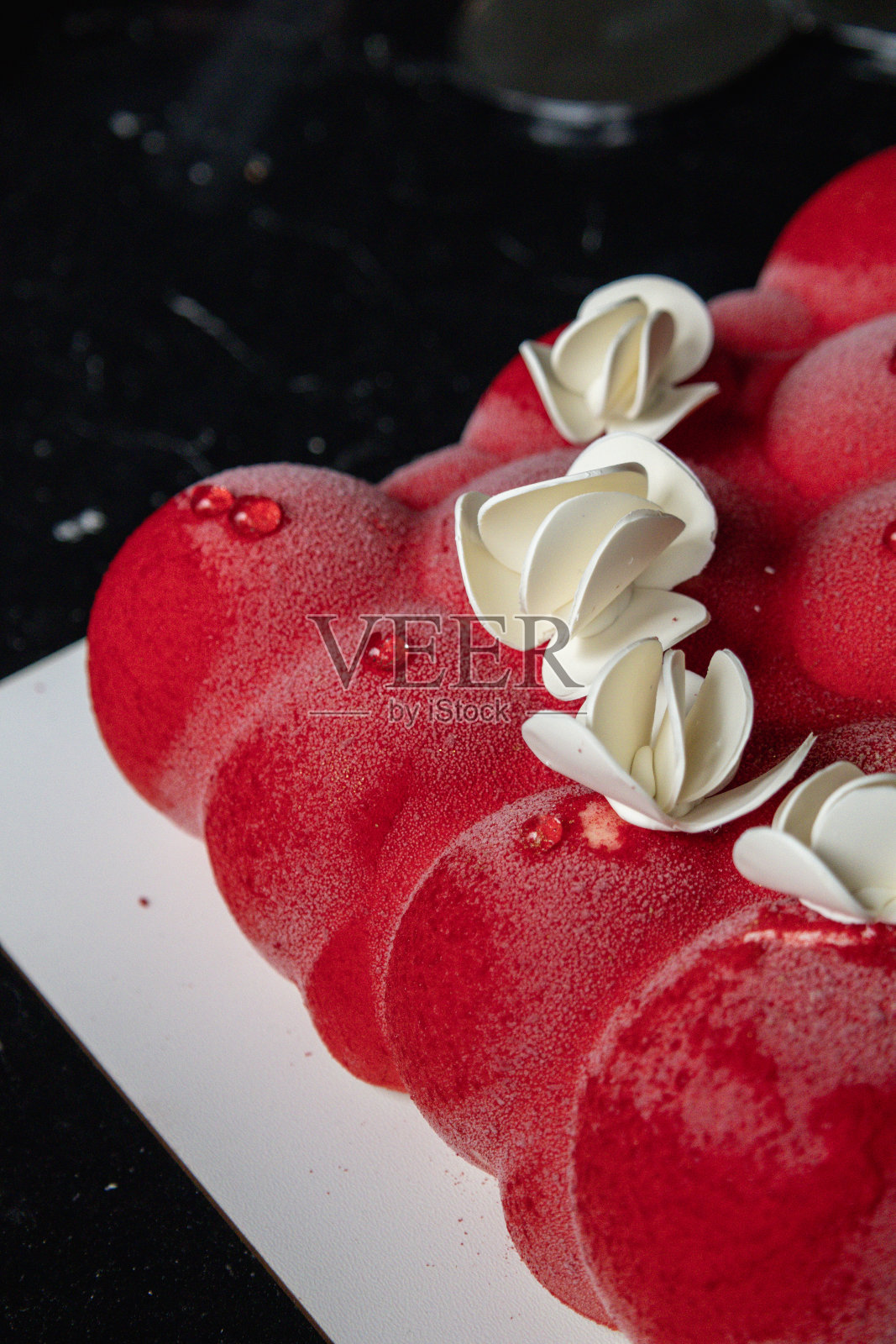 乌克兰基辅——2024年2月5日。漂亮的慕斯，小球形状的红蛋糕。上面是白巧克力花。他们给了我一个蛋糕作为生日礼物。照片摄影图片