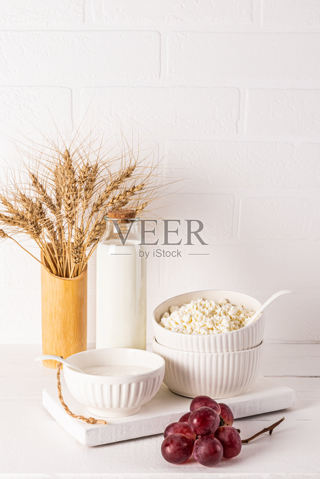 这是一幅美丽的静物画，为犹太节前节画的。白色垂直背景上的新鲜乳制品、葡萄串和面包穗。照片摄影图片