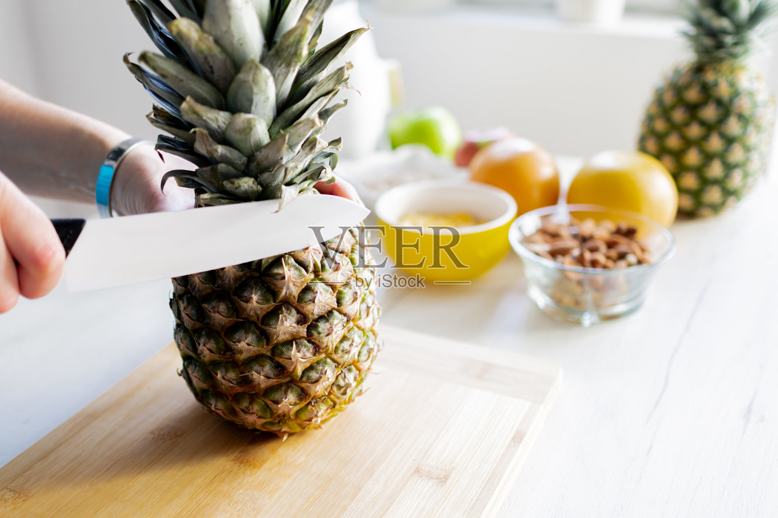 健康的食材，美味的早餐。菠萝，麦片，葡萄柚，苹果。女人的手在切新鲜的菠萝。照片摄影图片