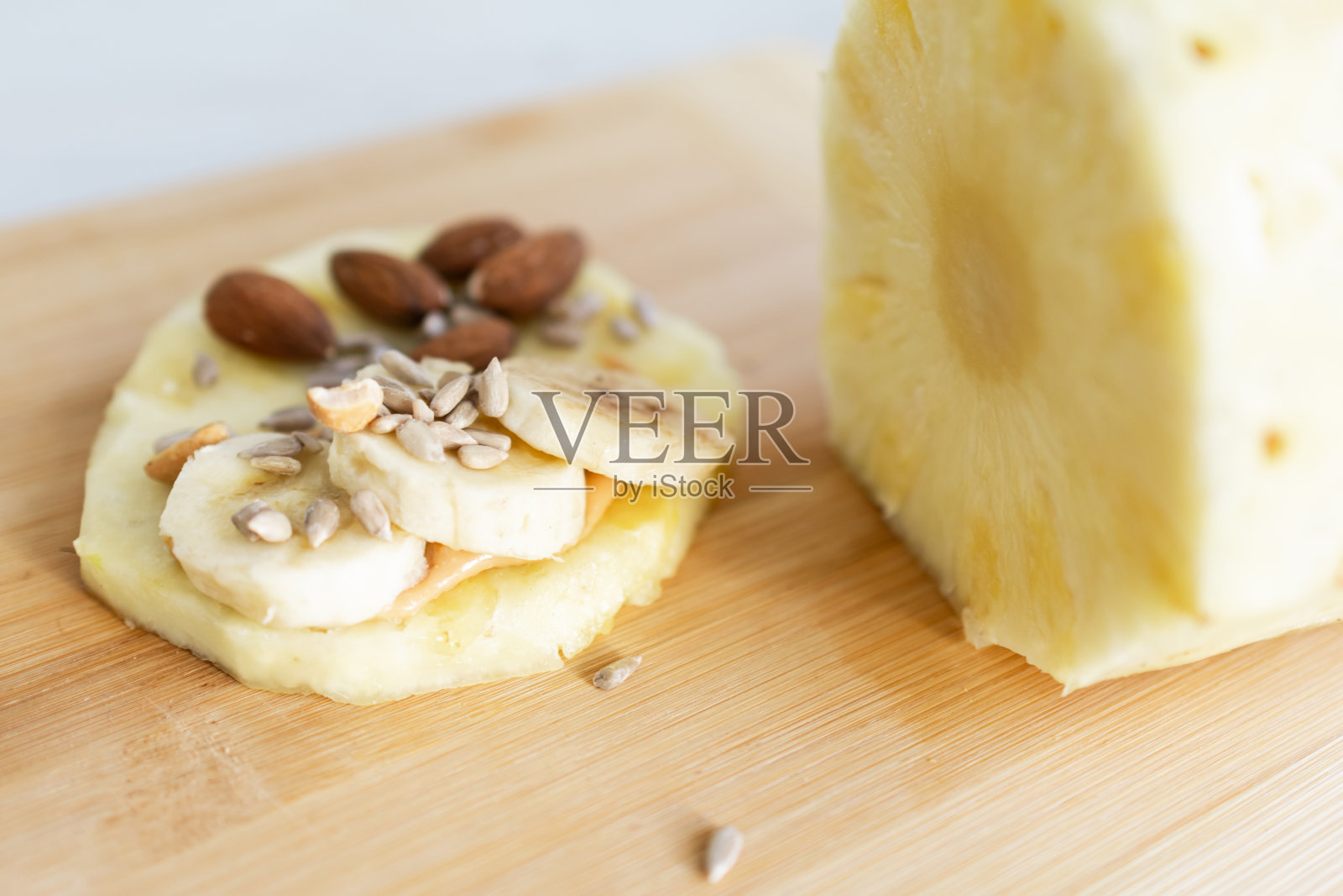 健康的食材，美味的早餐。菠萝切片配香蕉、花生、花生酱杏仁和葵花籽。照片摄影图片