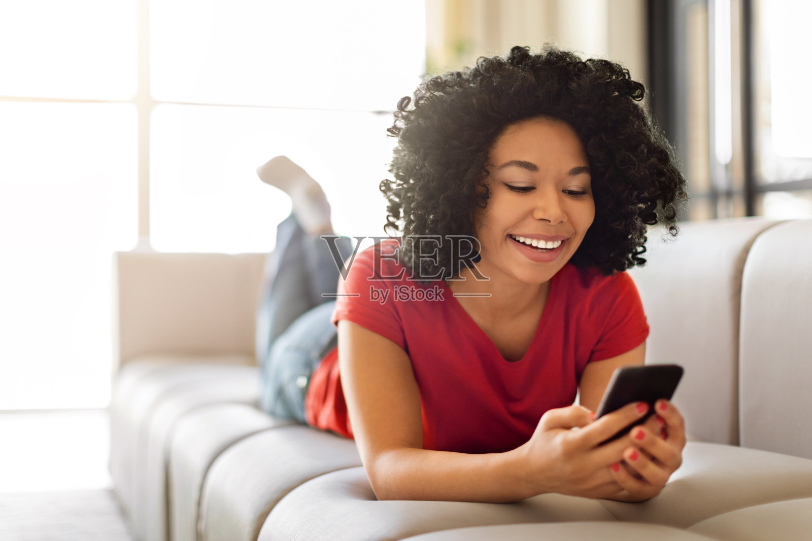 快乐的年轻黑人女性一边在家放松一边用智能手机发信息照片摄影图片