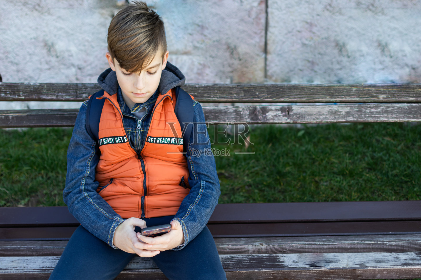 男生放学后要回家。他正坐在公园的长椅上。他正在和朋友进行视频通话。照片摄影图片