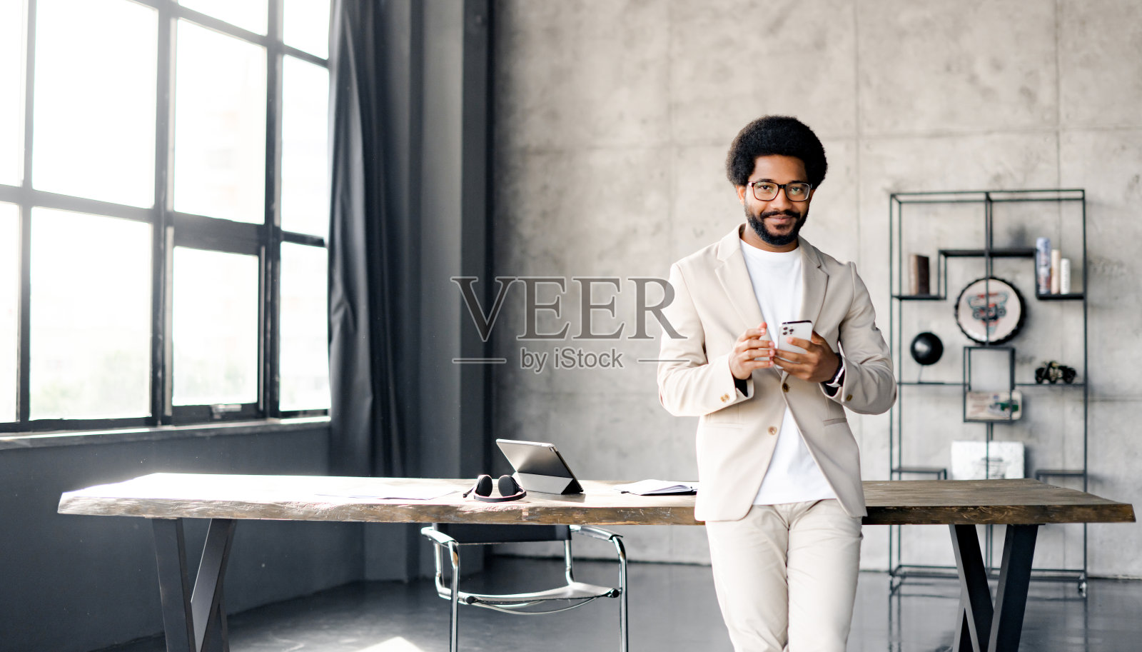 一位兴高采烈的巴西商人，穿着漂亮的休闲米色西装，坐在阁楼办公室里照片摄影图片