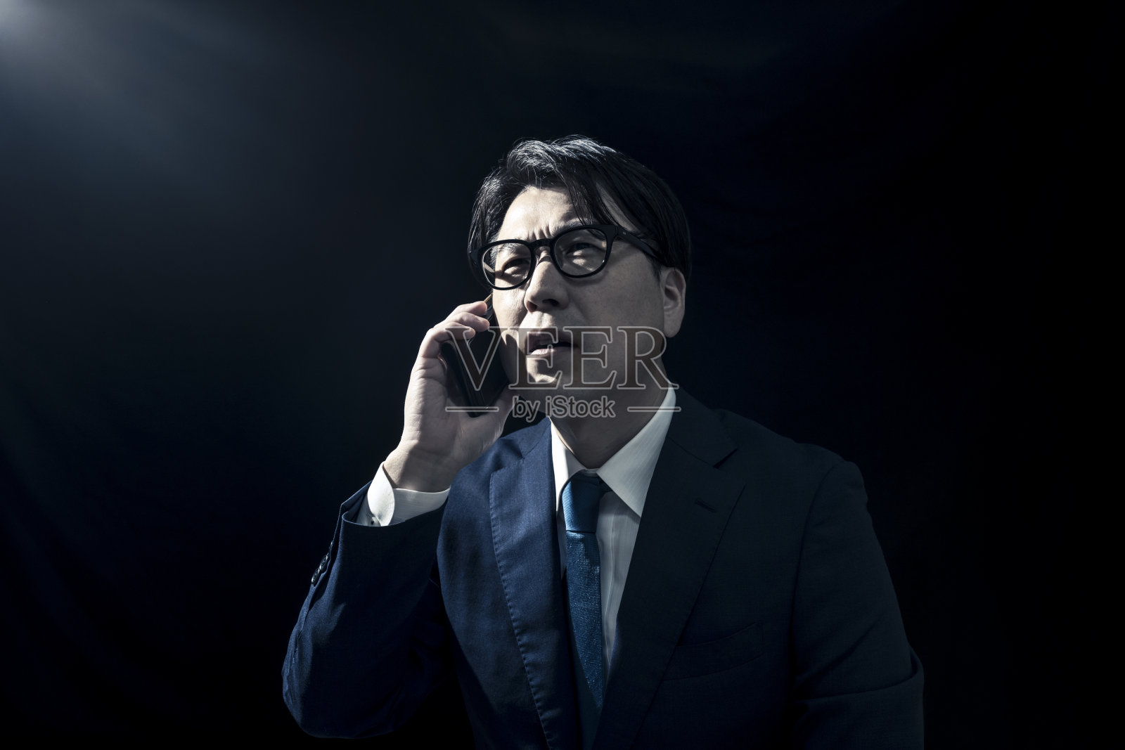 西装革履的商人在昏暗的房间里用智能手机打电话照片摄影图片