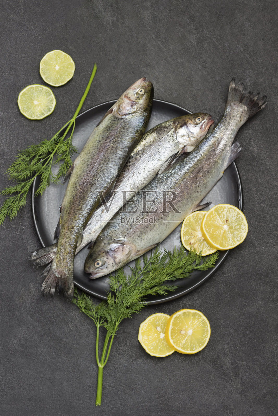 生鳟鱼配柠檬角和莳萝，黑色盘子。照片摄影图片