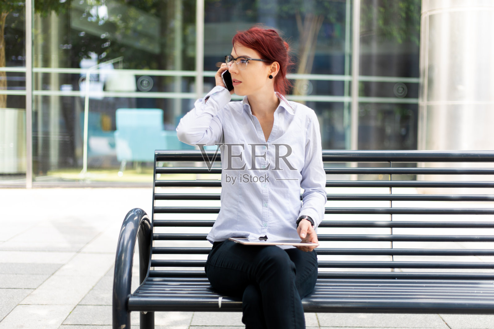 微笑着的女商人在户外坐在长凳上用数码平板电脑打电话照片摄影图片