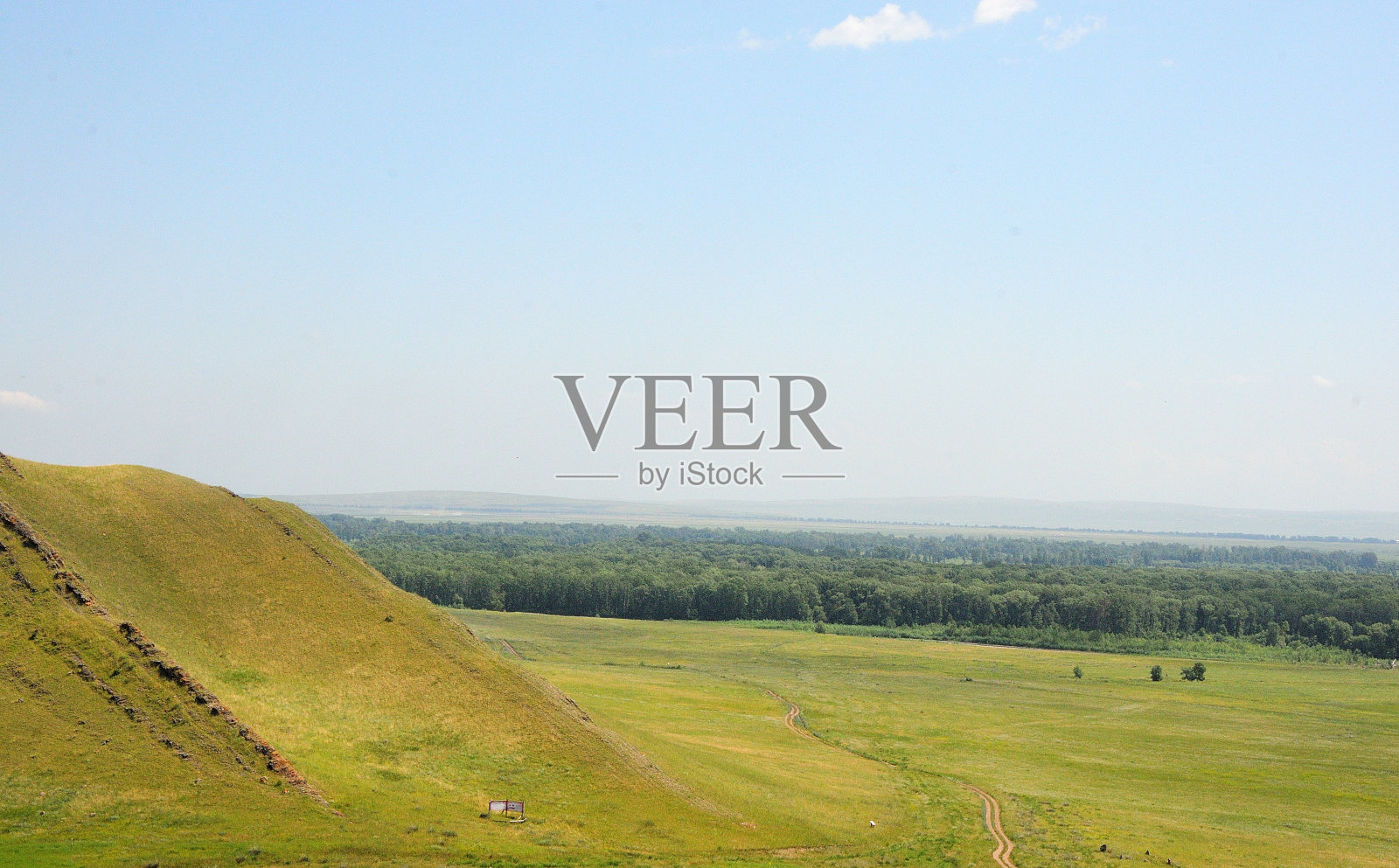 在一个阳光明媚的夏日，在一望无际的草原边缘，一座高山的斜坡上有不寻常的石头结构。照片摄影图片