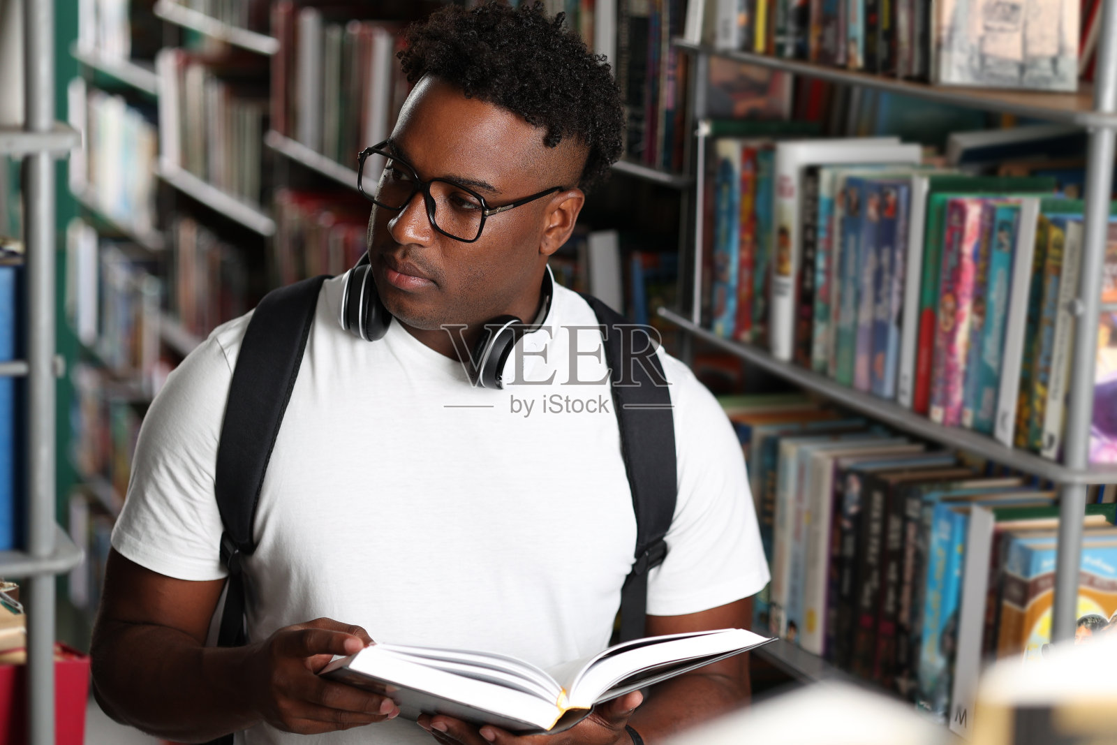 穿着便服的年轻黑人图书管理员背着背包清理书架照片摄影图片