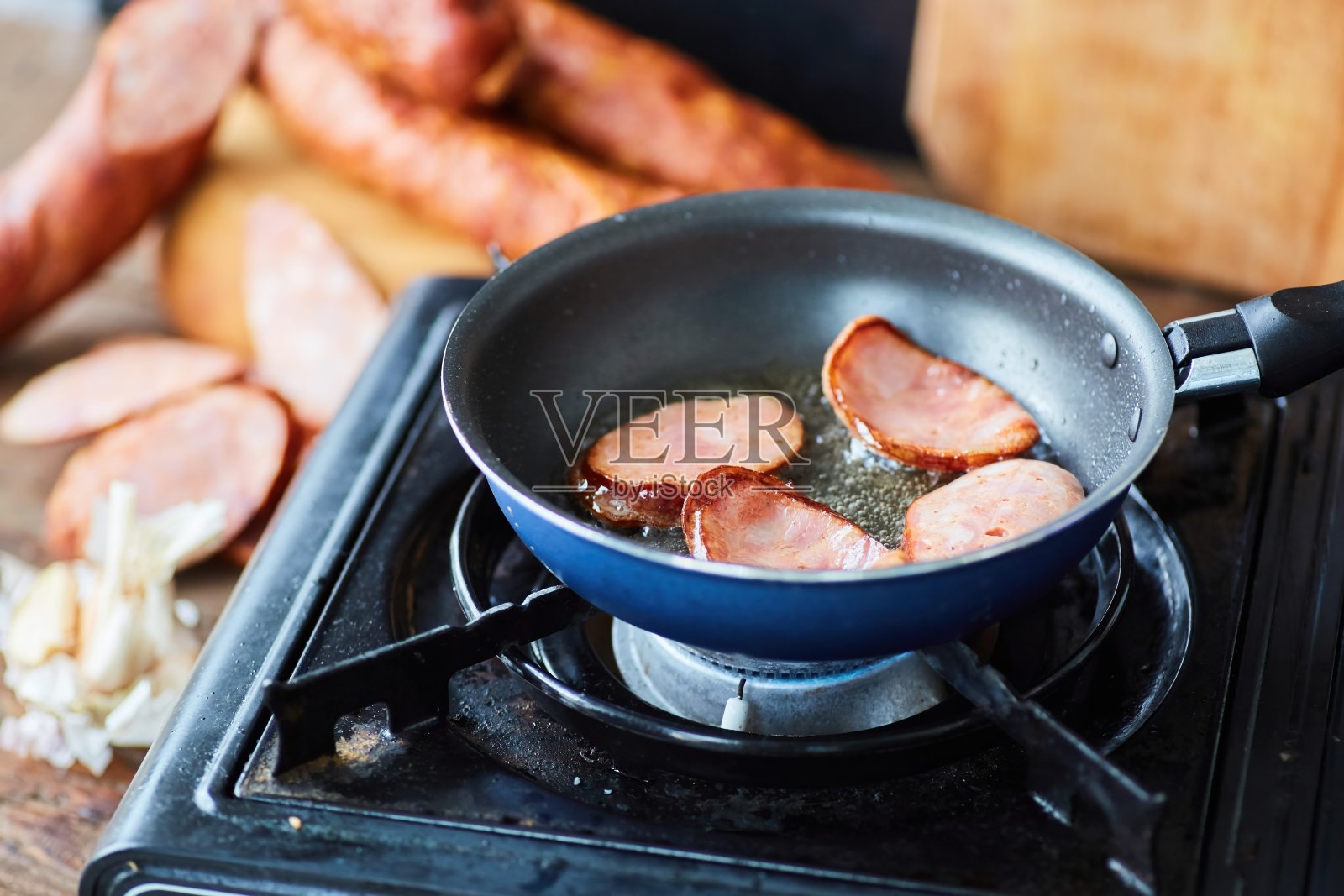 一步一步烹饪这道菜。一块块香肠在平底锅里放在野营炉上煎。照片摄影图片