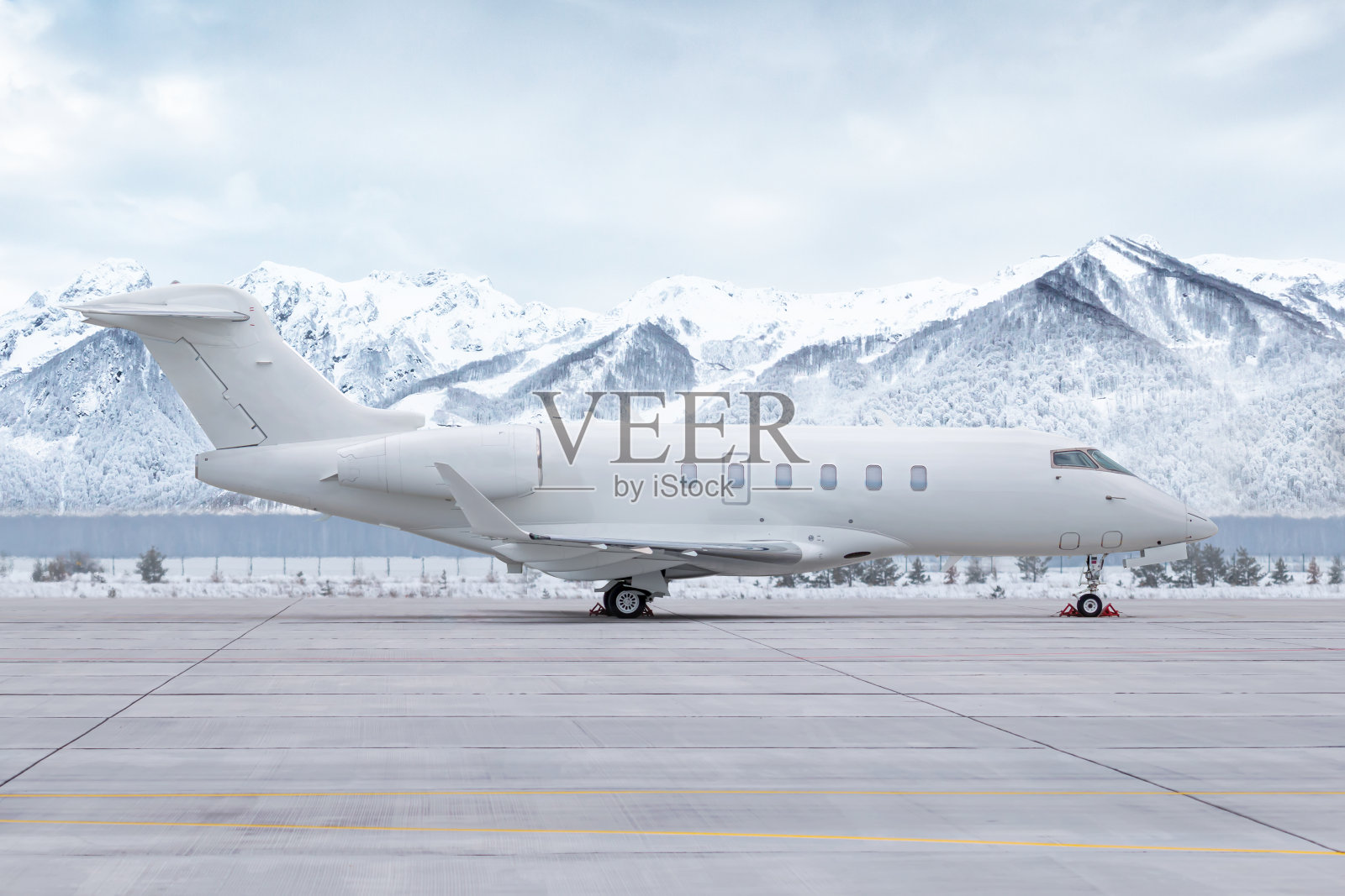 现代白色私人飞机停在机场停机坪上，背景是风景如画的雪山照片摄影图片