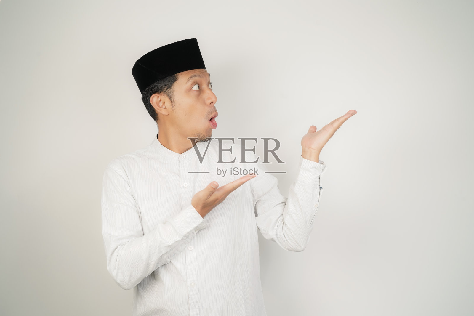 哇，一名身穿阿拉伯服装的亚洲穆斯林男子用手指着孤立背景上的空白照片摄影图片