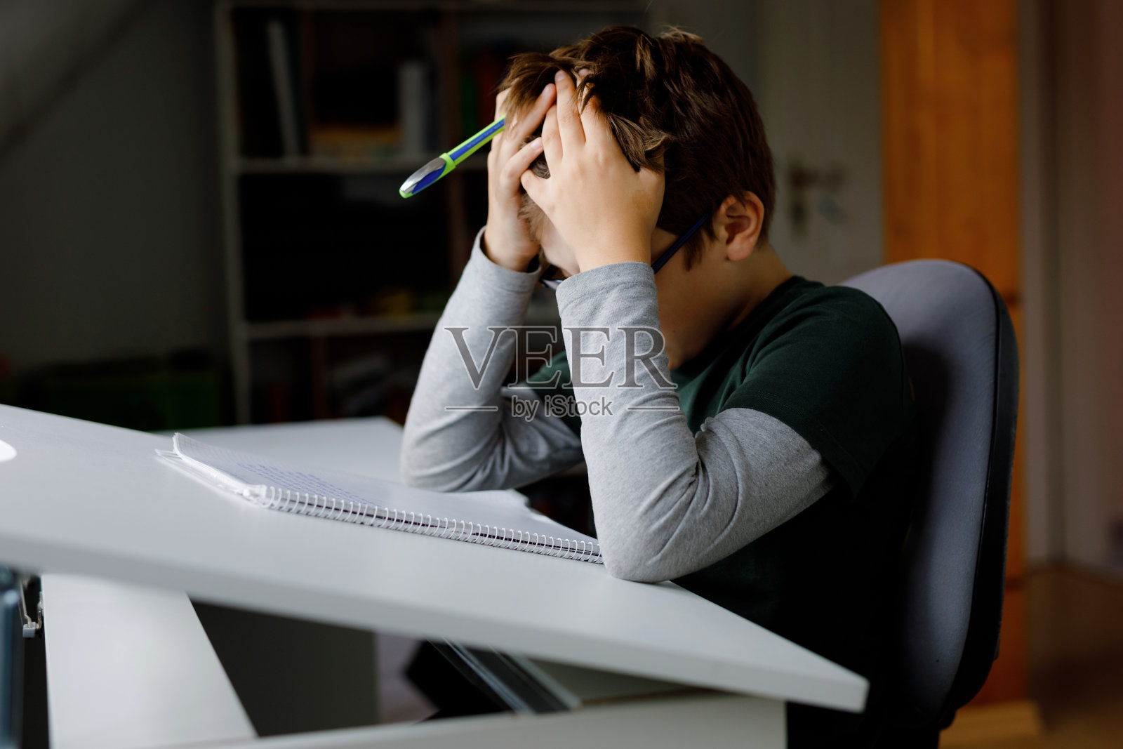 在冠状病毒大流行的隔离期间，勤奋悲伤的小学生正在做作业。在冠状病毒疫情期间，孩子对在家上学感到沮丧，学校关闭了。照片摄影图片